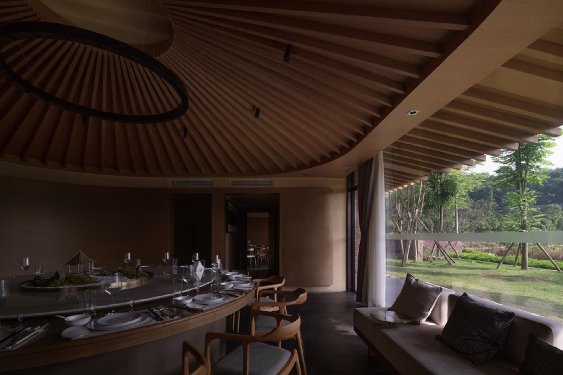 Cozy restaurant interior with a dining area and living room featuring a round table, chairs, couch, and bench, with wine glasses and a warm atmosphere