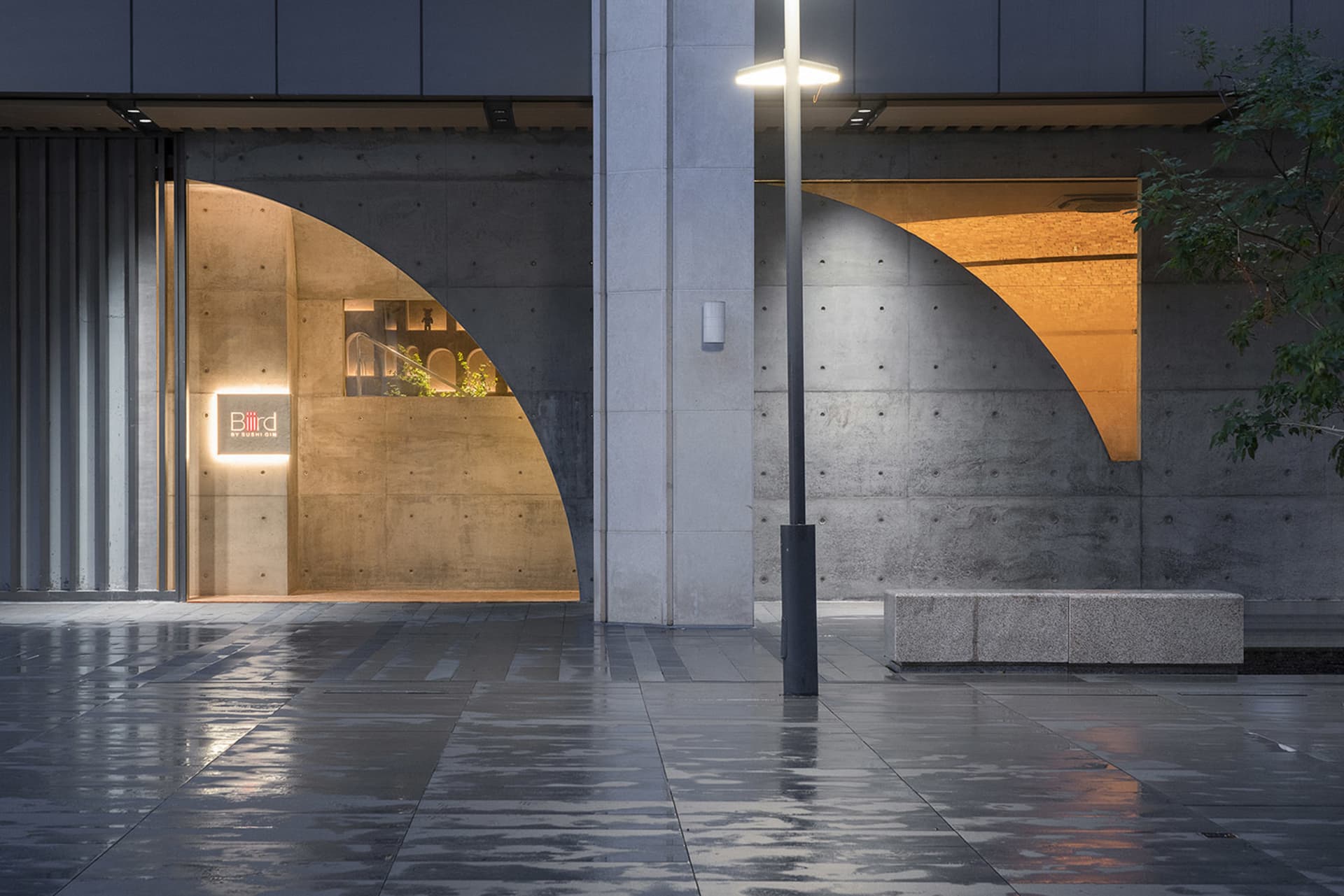 A modern building with two large concrete arches on either side of its entrance, featuring a bench and a contemporary design that balances functionality and aesthetics