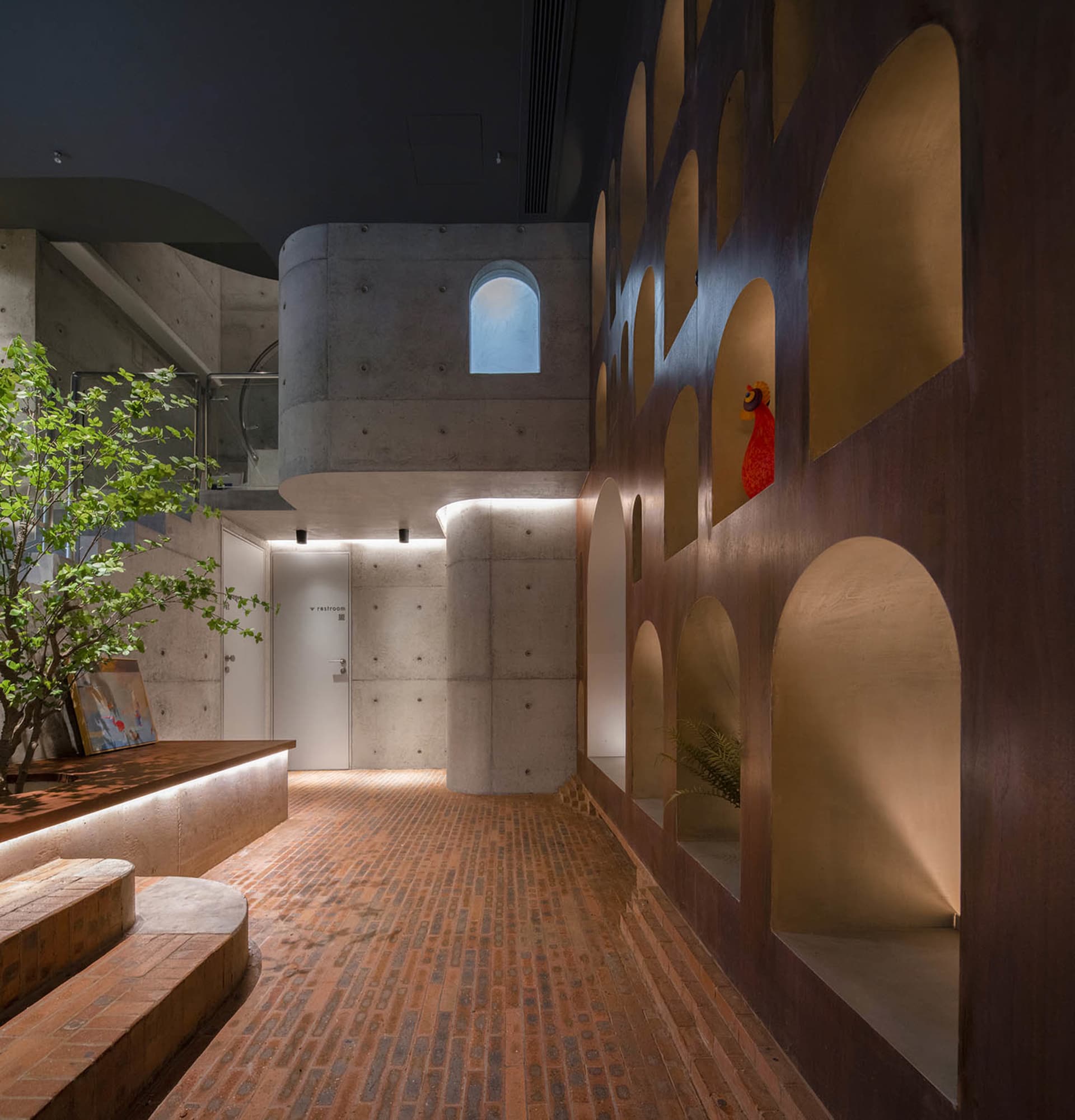 Open industrial space with a brick floor, concrete walls, and natural light from several windows, featuring a bird perched on the wall