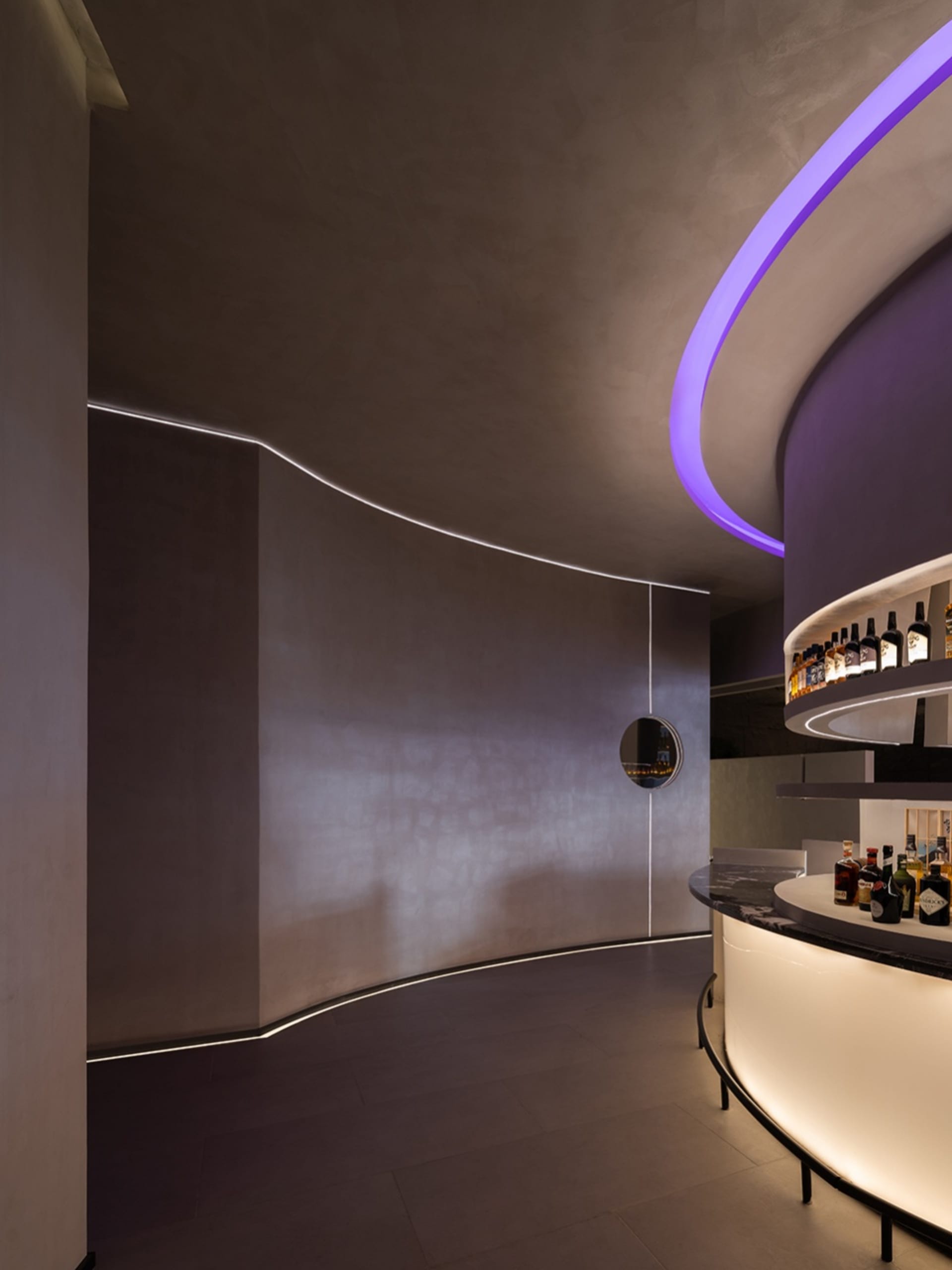 Dimly lit bar with a wooden counter and a circular clock on the wall, surrounded by bottles of alcohol