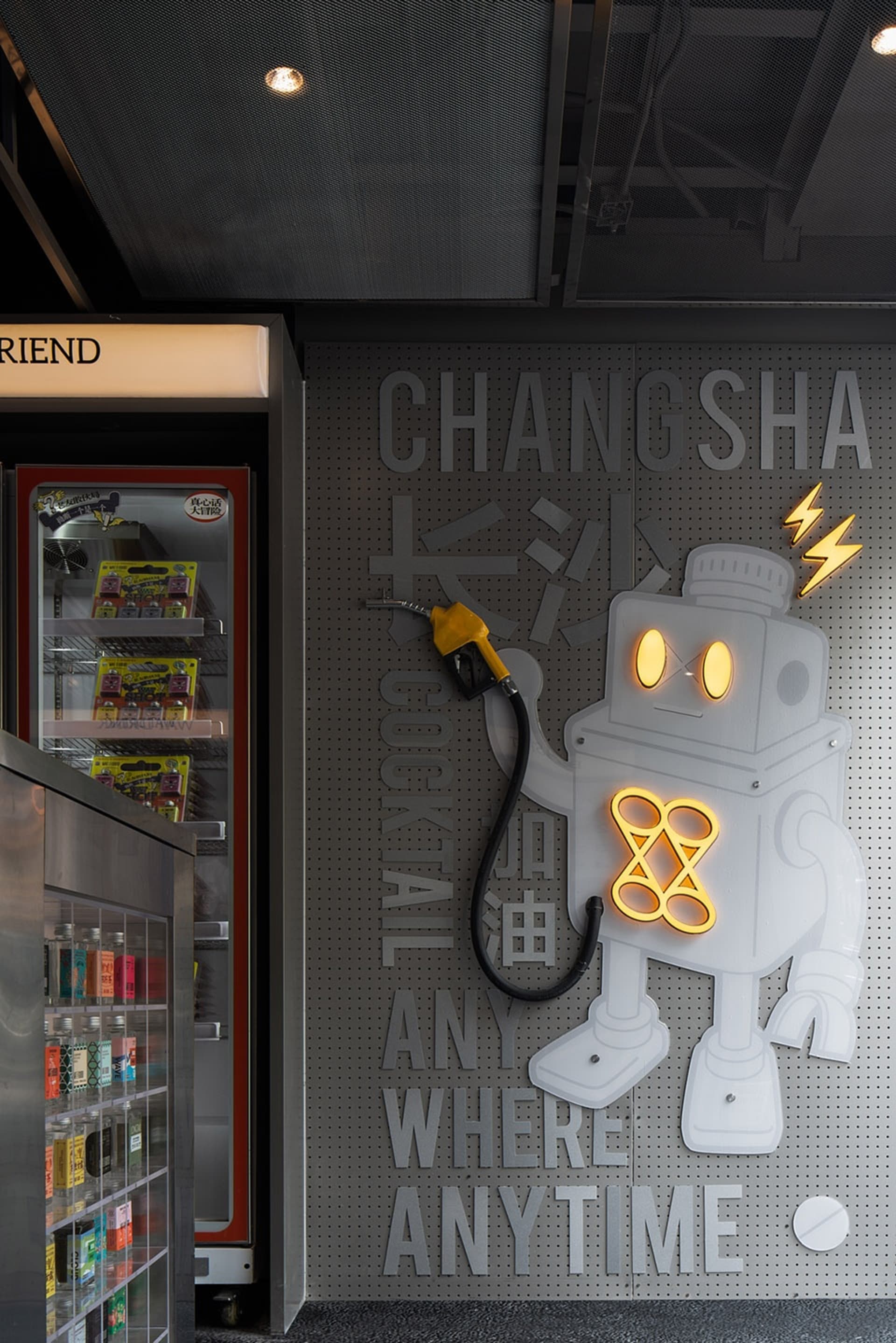 A futuristic retail store with a robot holding a gas pump, a refrigerator, and vending machines, surrounded by bottles and modern decor
