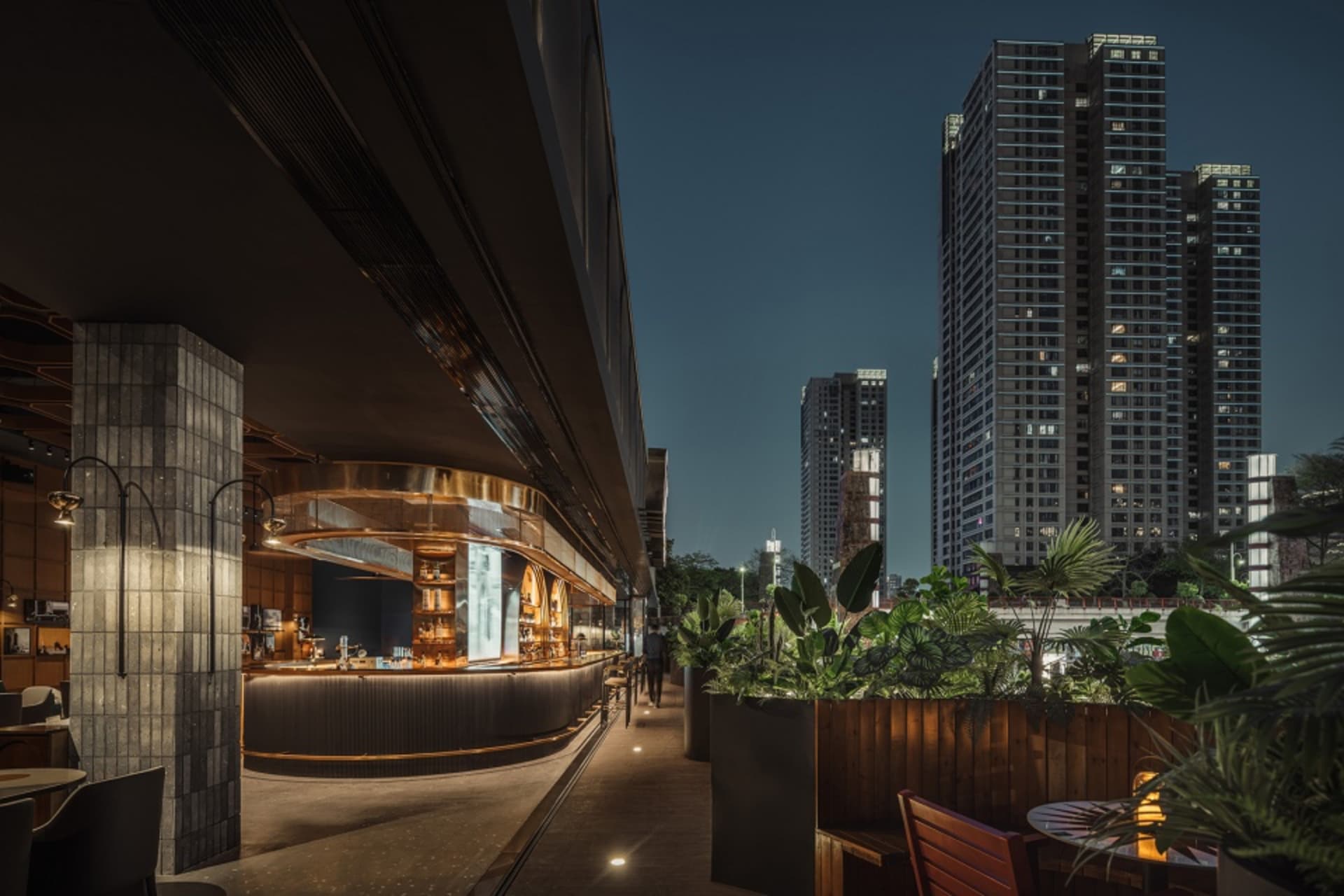 A bustling city street at night with tall buildings, potted plants, and chairs, evoking a sense of grandeur and urban life