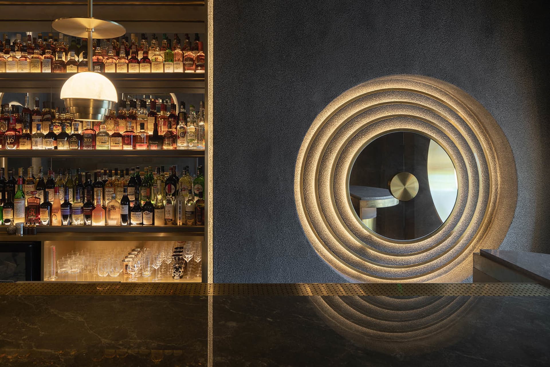 A sophisticated bar area with a large mirror, wine bottles, and wine glasses, creating a sense of depth and luxury