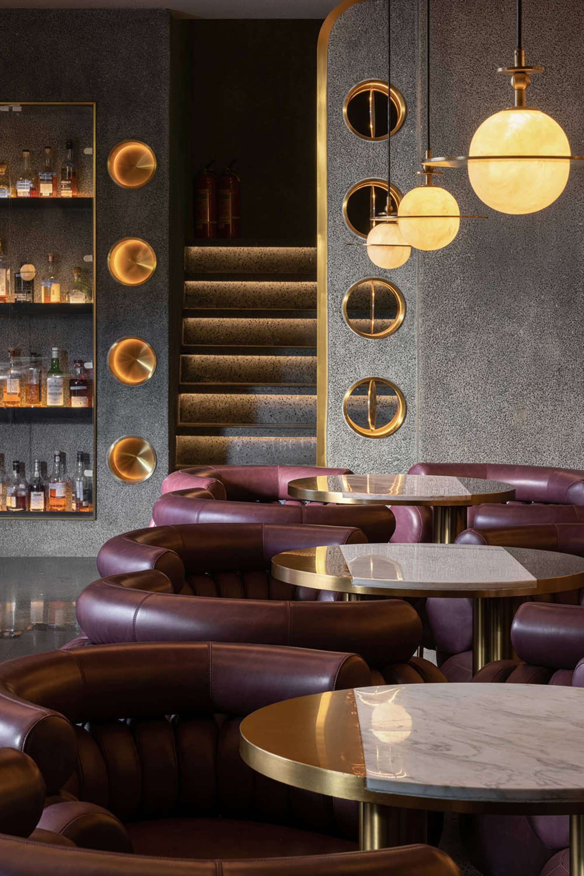 Cozy restaurant interior with a bar area, tables, chairs, and bottles, featuring a combination of marble and wood elements and warm lighting