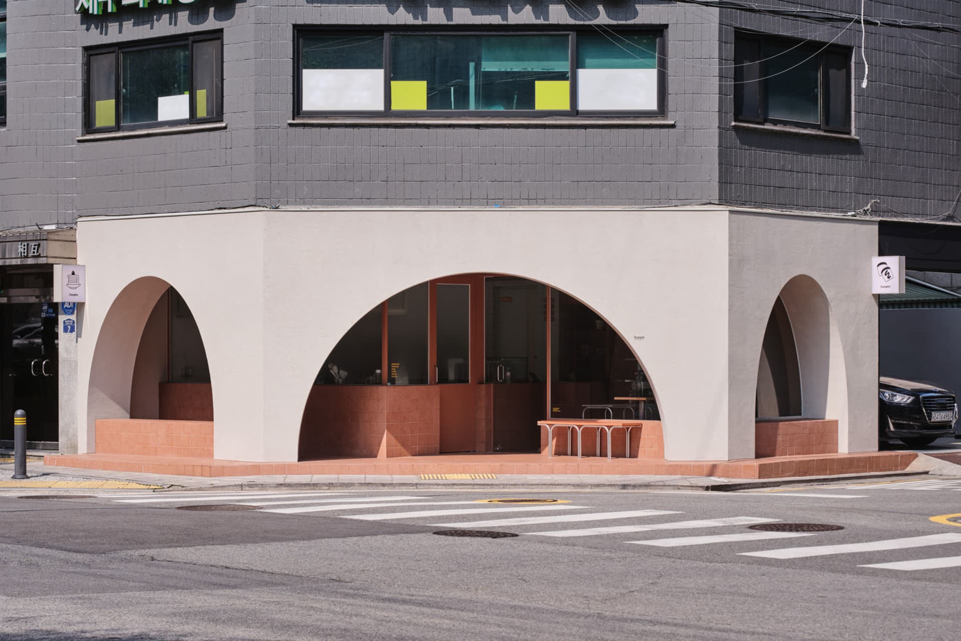 Gray concrete building with two arches and outdoor seating area with chairs and dining tables