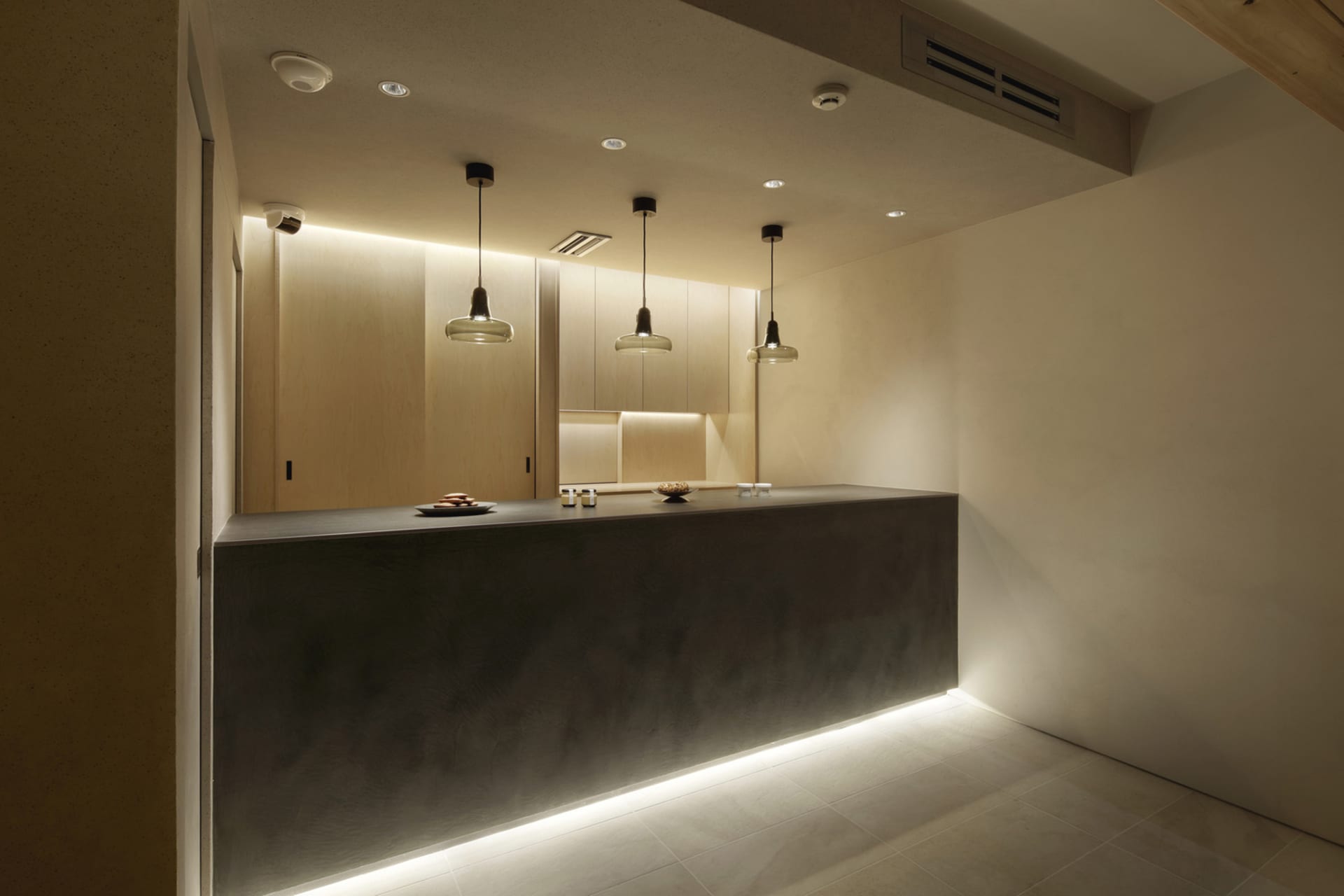 Empty kitchen with a gray countertop, white walls, and overhead lighting, featuring a sink and modern cabinets