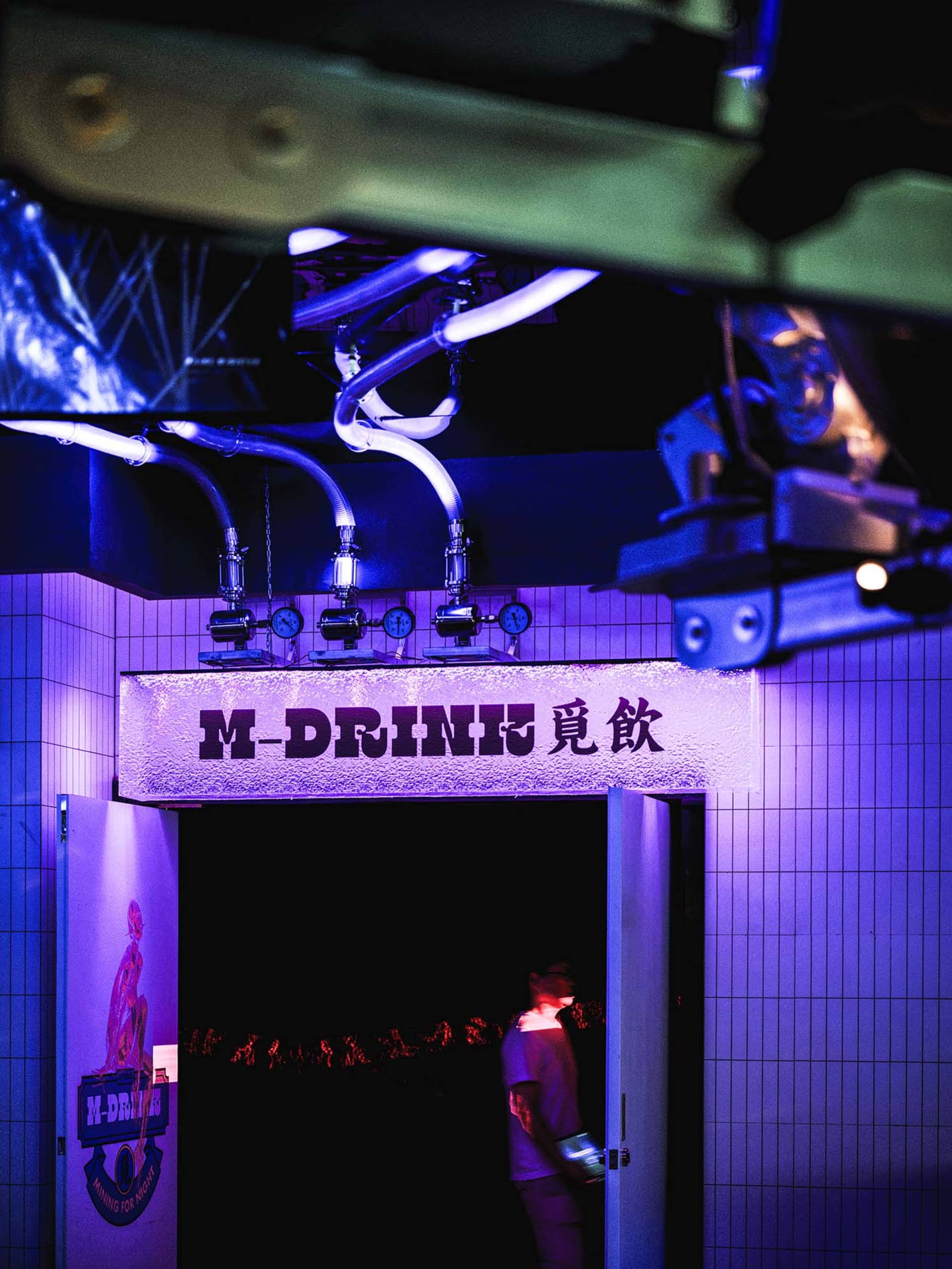 A lively Asian bar with purple lights, patrons standing near the entrance and scattered throughout the space
