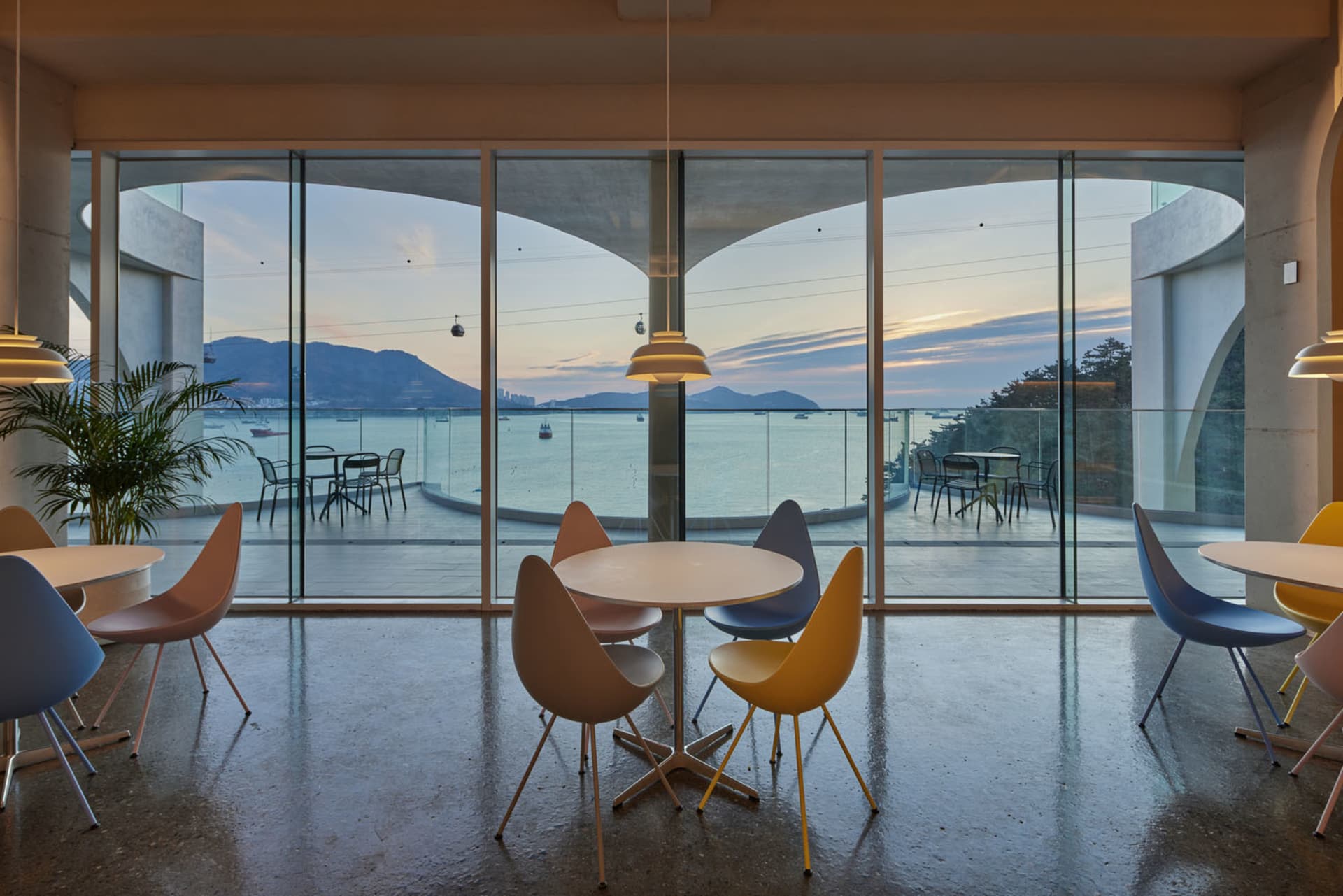 Dining area with a large window offering an ocean view, featuring a white table and various chairs with a yellow seat in a modern and inviting atmosphere