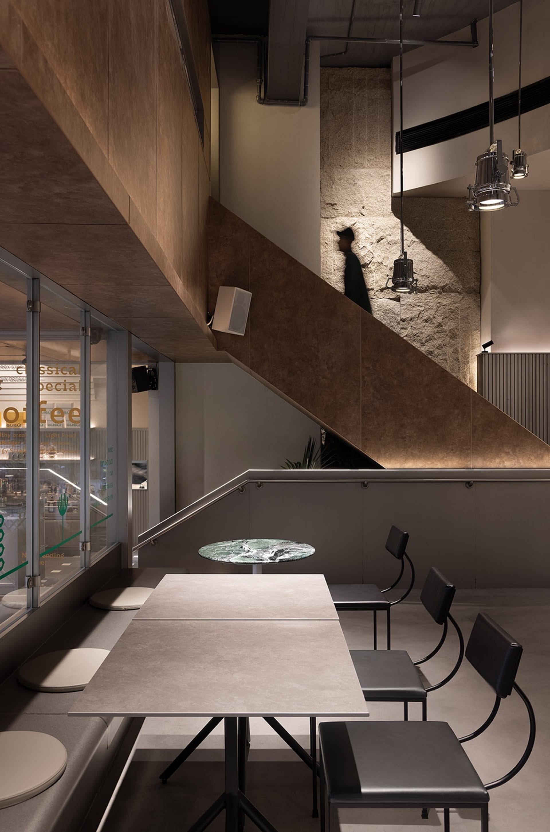 A cozy coffee shop with a staircase, chairs, a dining table, and a potted plant, creating a welcoming atmosphere