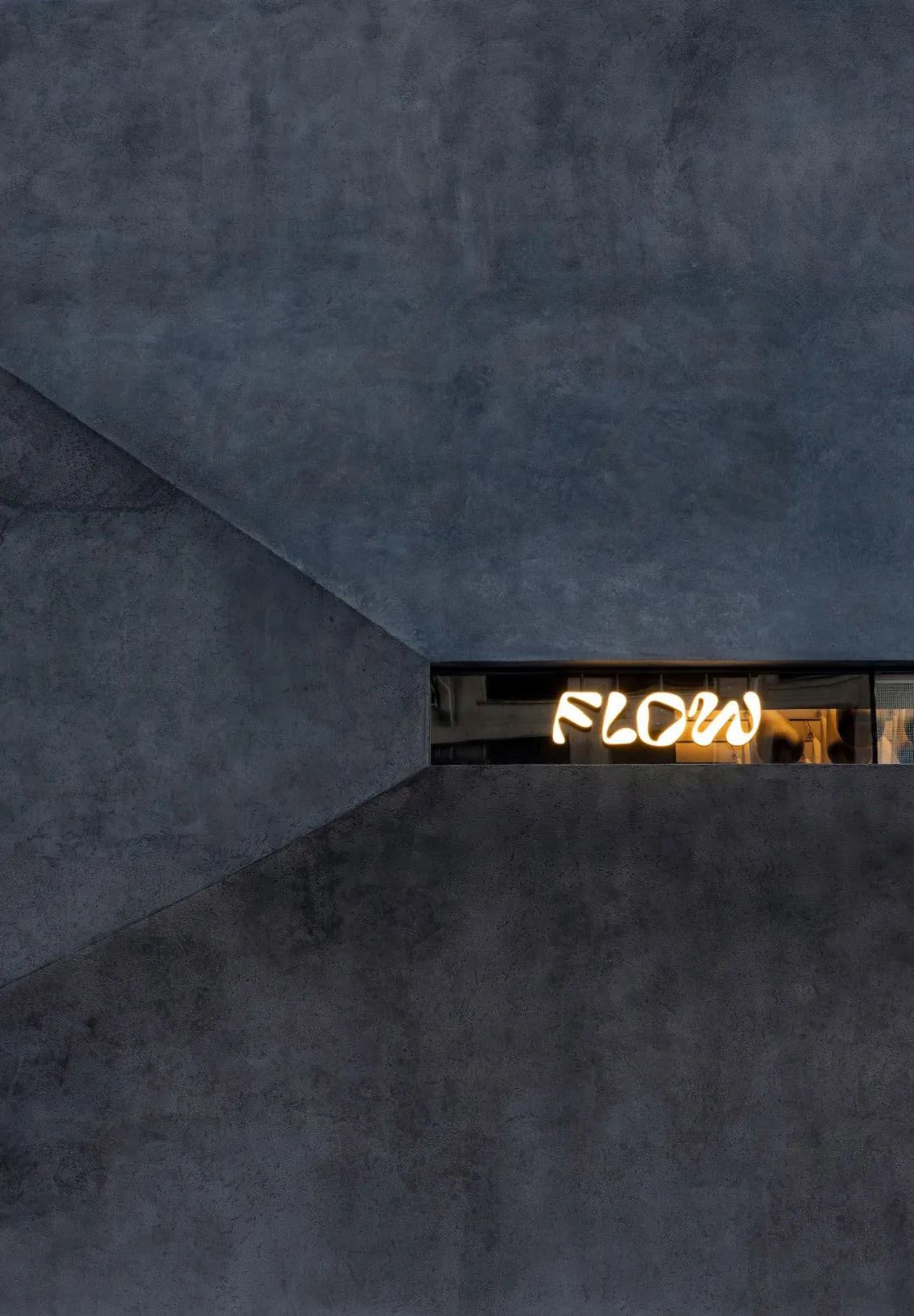 Modern building with a lit window featuring the word flow, set in a contemporary urban environment