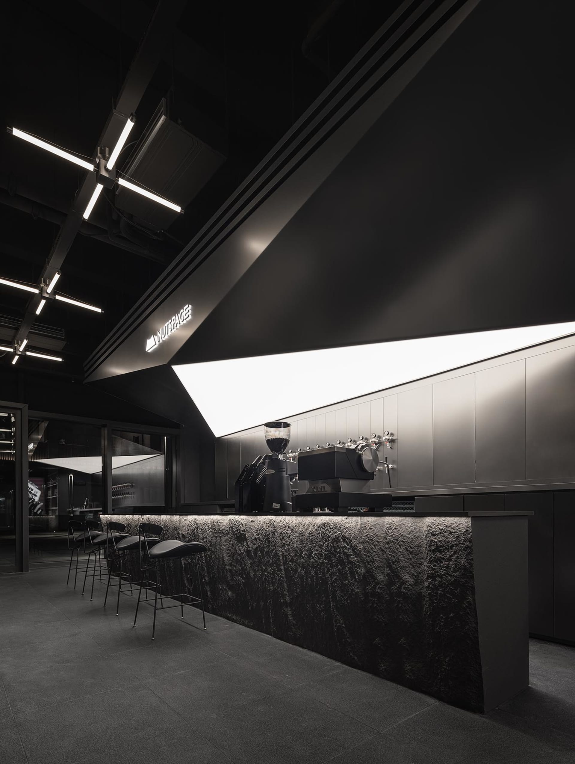 A modern bar area with a black countertop, coffee machine, and two chairs, well-lit by overhead lights