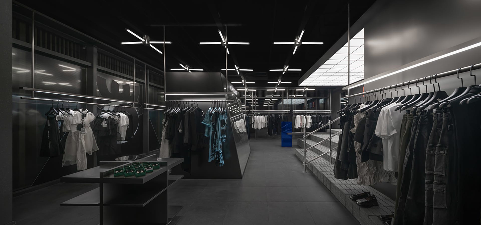 A dark and empty retail space with white walls and a black ceiling, featuring clothing racks and a minimalist layout