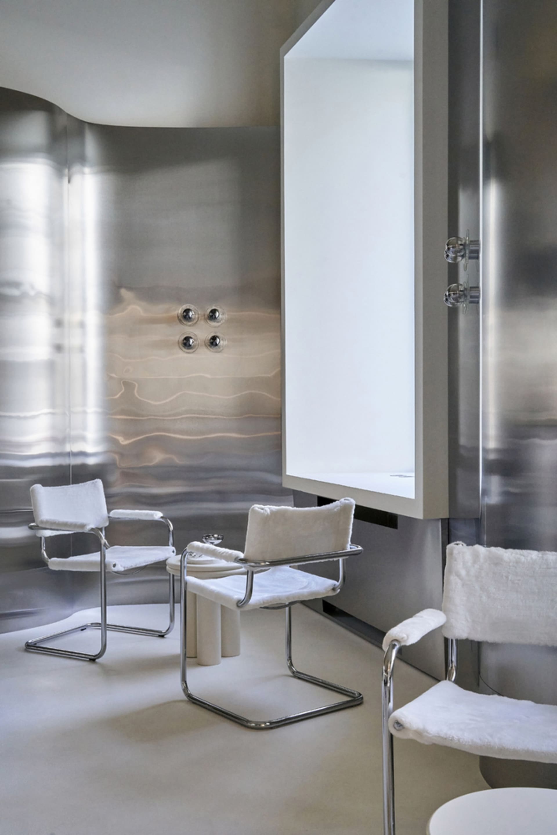 A minimalist bathroom with a large mirror, two chairs, and a sink, featuring a clean and white design
