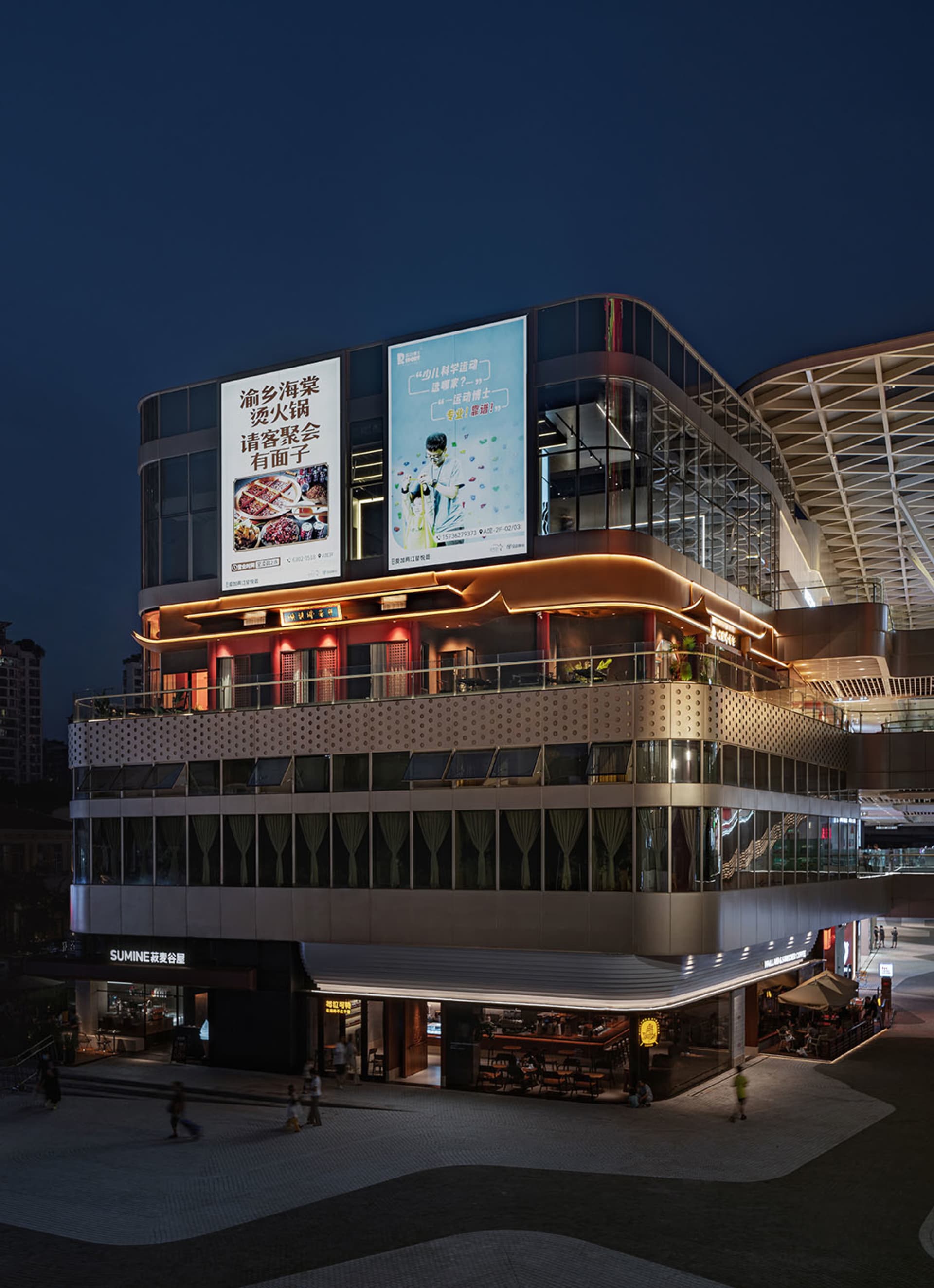 A modern Asian building at night with a large glass structure, illuminated by artificial lights, and a prominent sign on its side