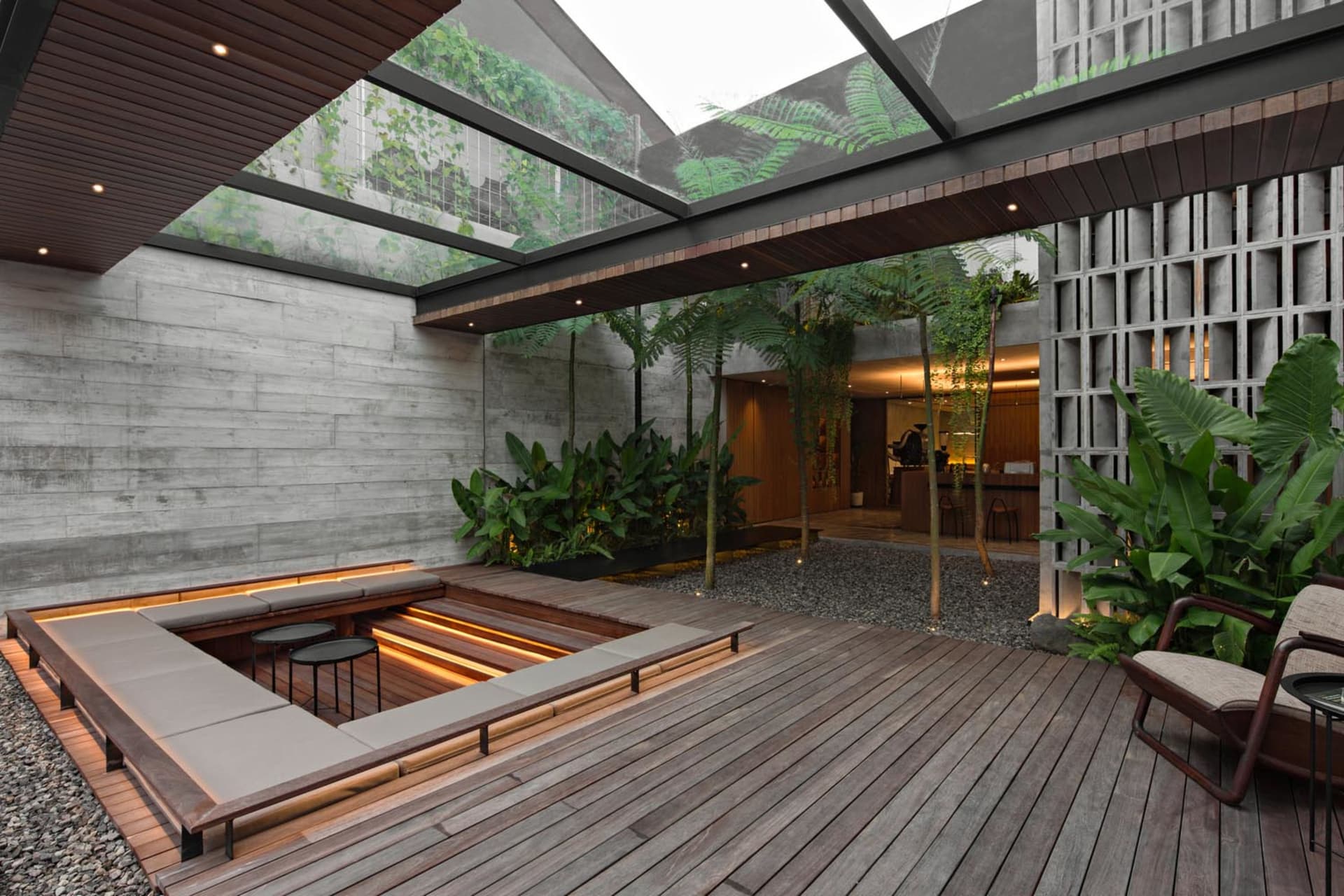 A warm and inviting outdoor living space with a large wooden deck, glass ceiling, benches, chairs, and potted plants