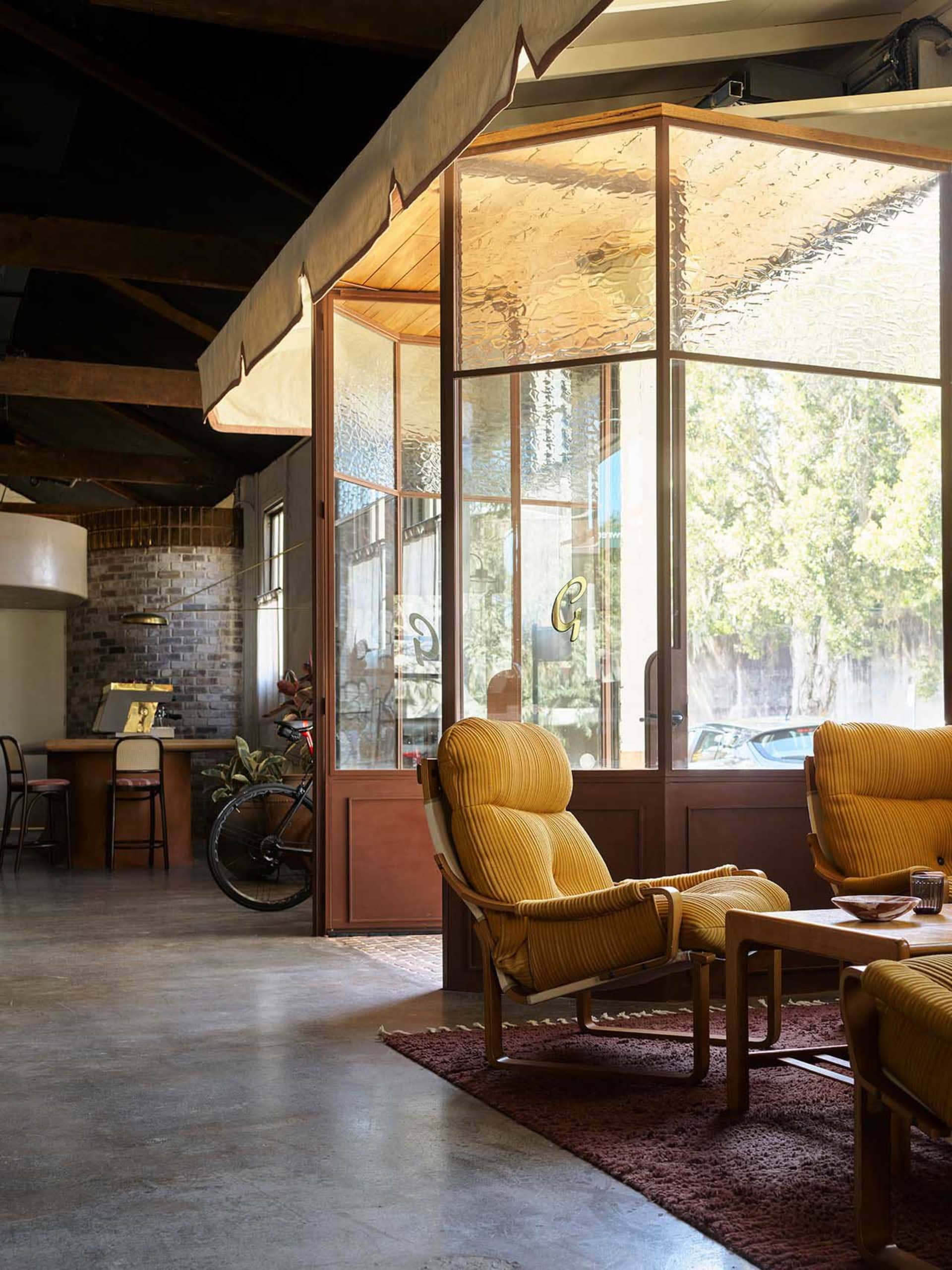 A modern living room with a yellow chair, dining table, couches, and a potted plant, well-lit by natural sunlight