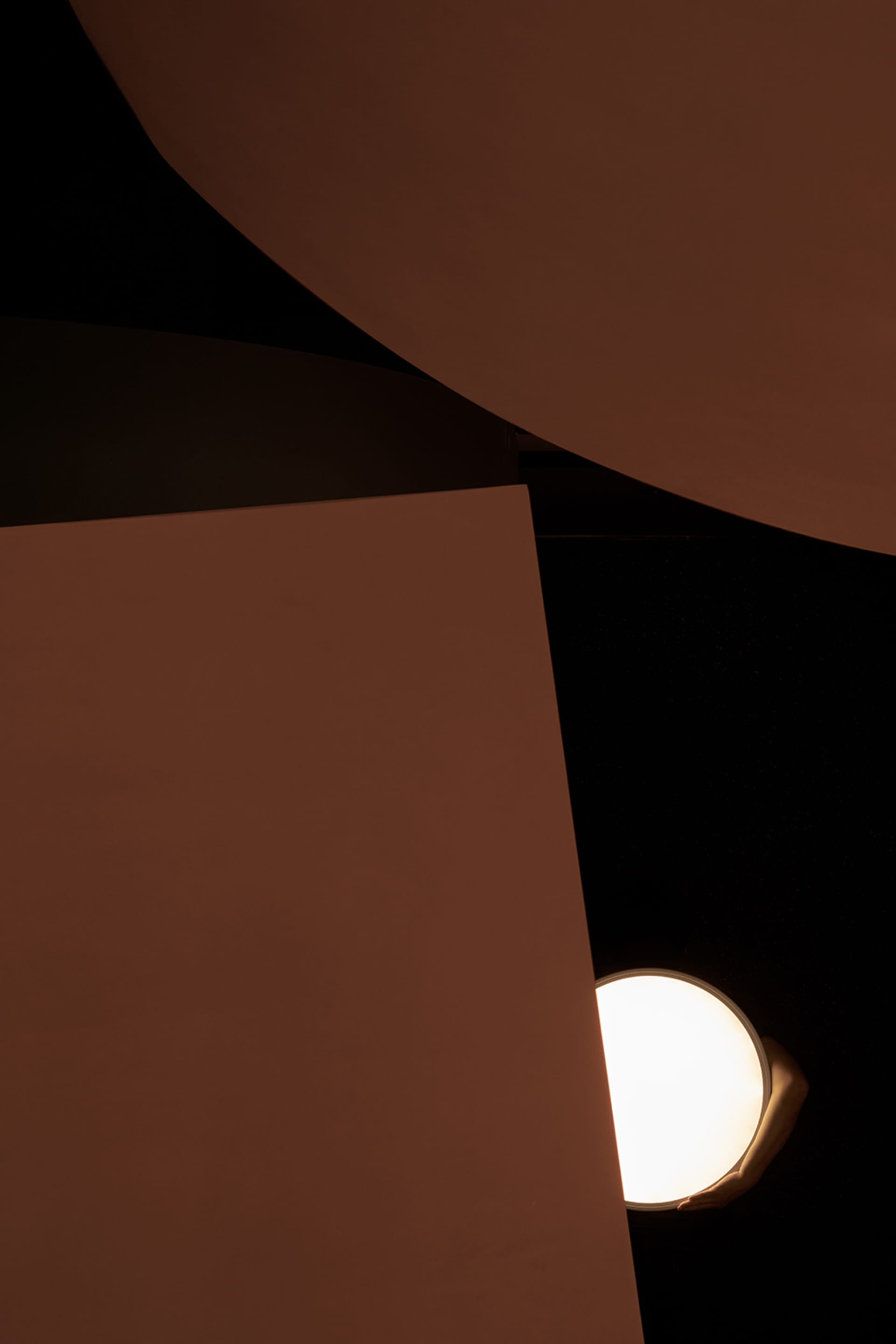 A dimly lit interior space with a large white wall and a round object on display, lit by two lights on either side