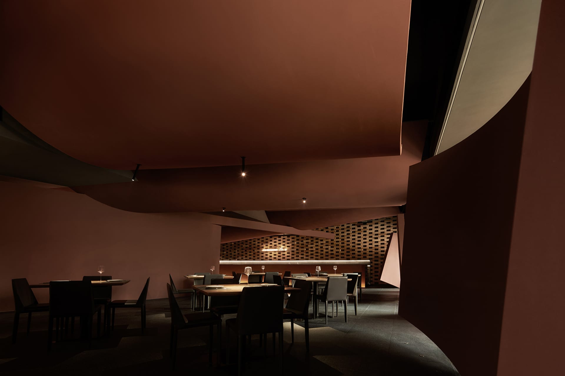 Dimly lit restaurant with red accents, pink walls, and chairs placed near tables