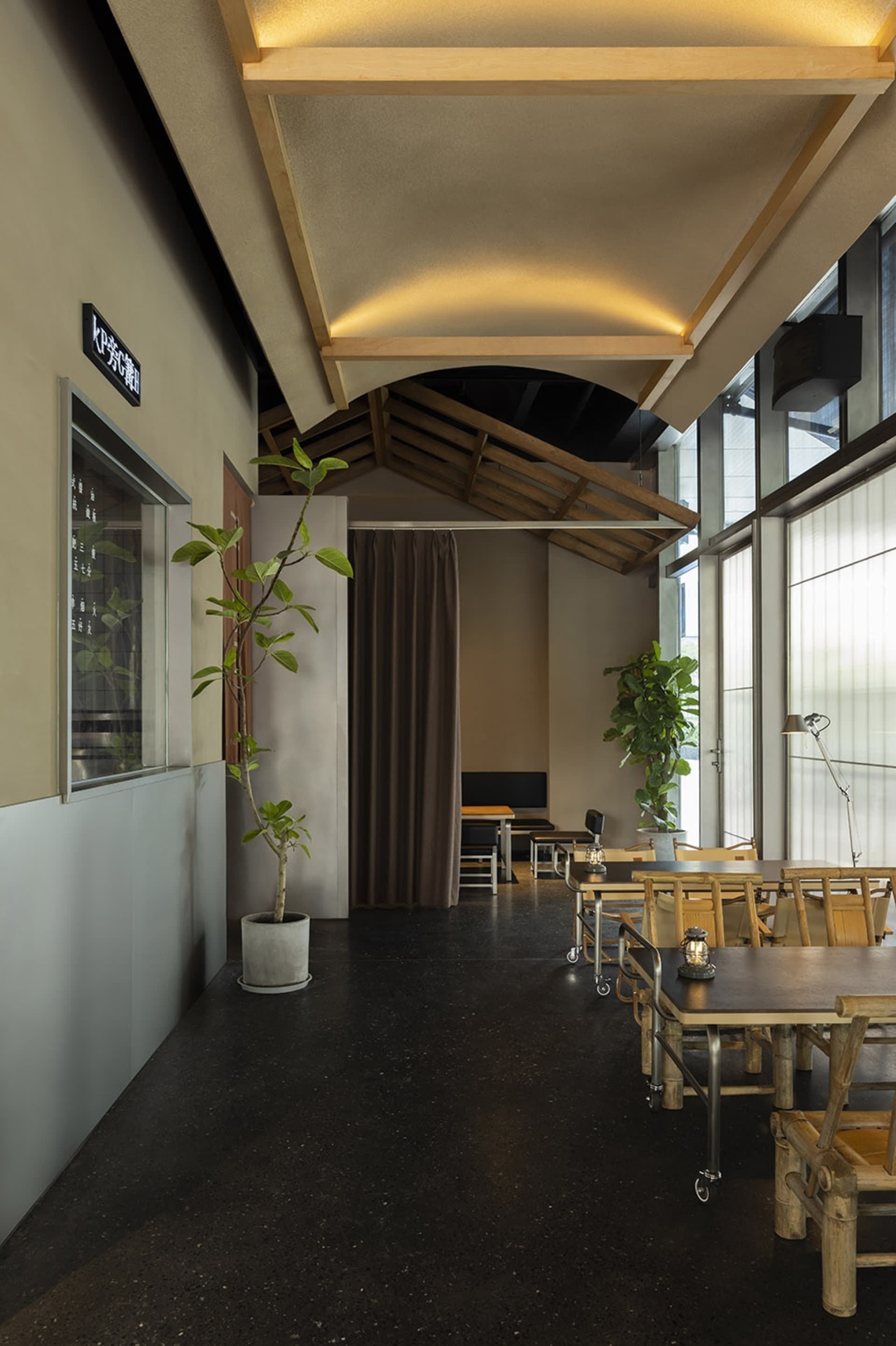 A well-lit dining area with wooden tables and chairs, surrounded by potted plants, creating a comfortable and inviting atmosphere