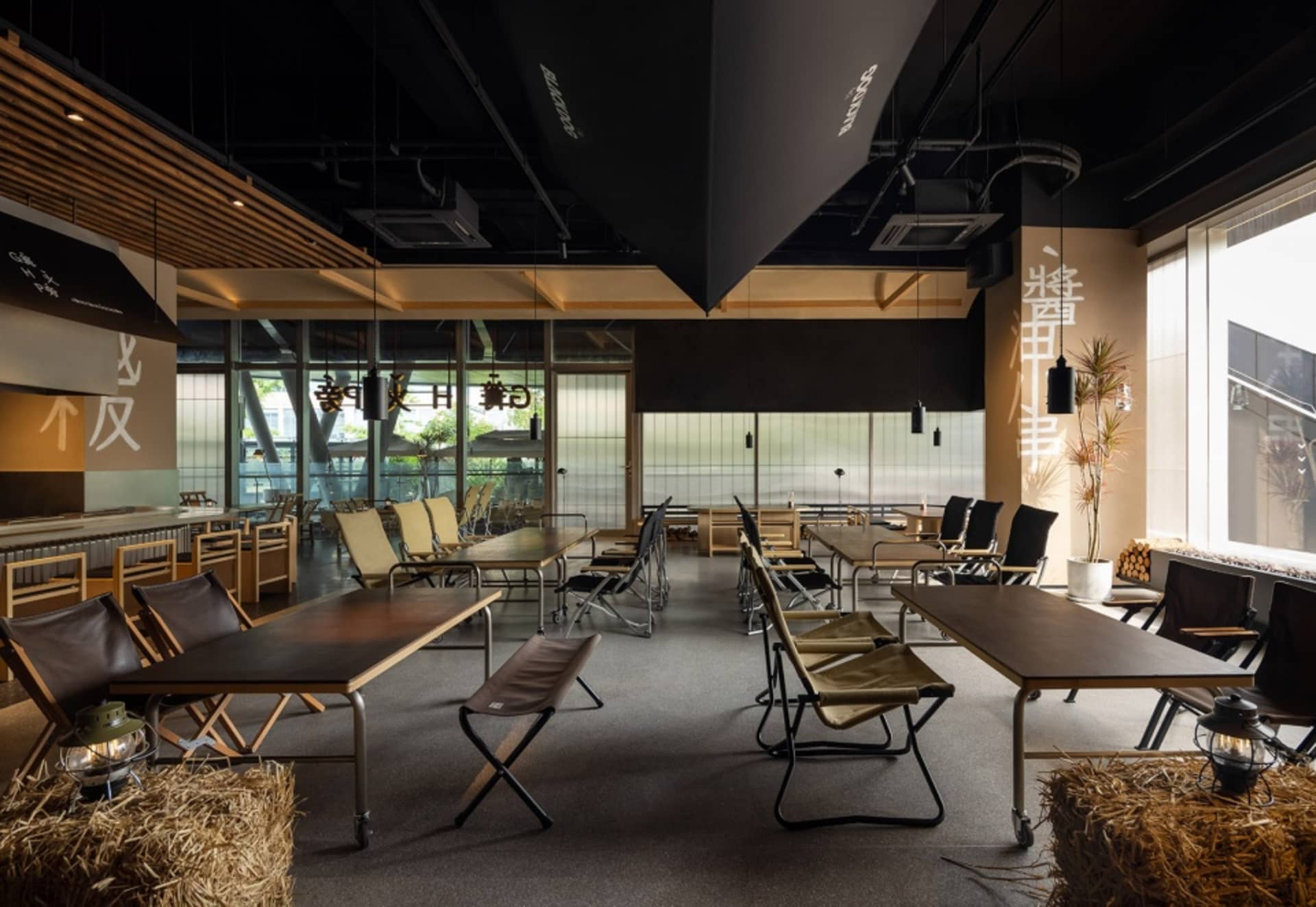 A modern restaurant dining area with black ceiling, featuring multiple tables and chairs arranged throughout the space, creating a comfortable and inviting atmosphere