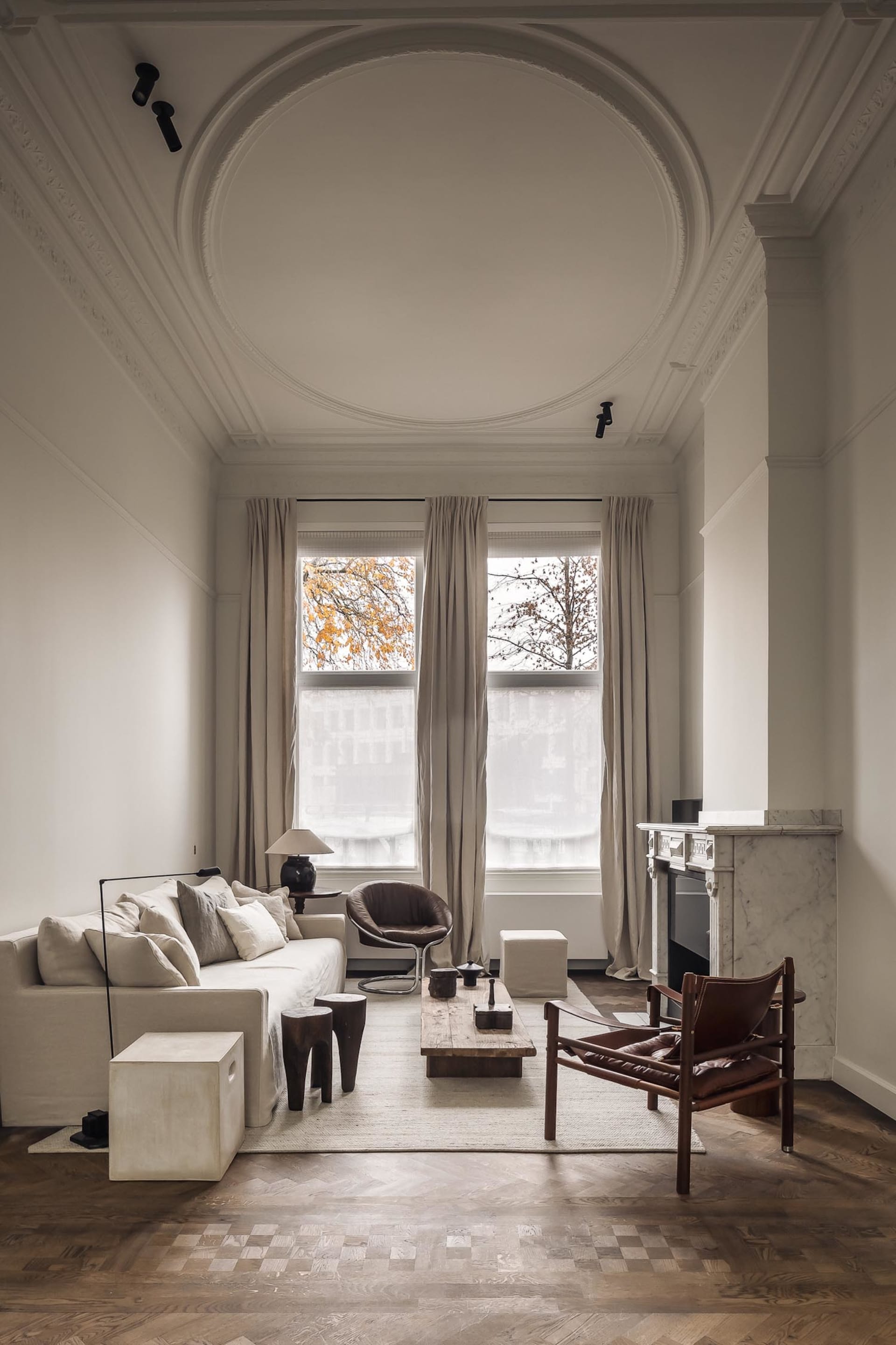 Modern living room with a white interior, wood furniture, and a fireplace, featuring two windows and a clean, bright atmosphere