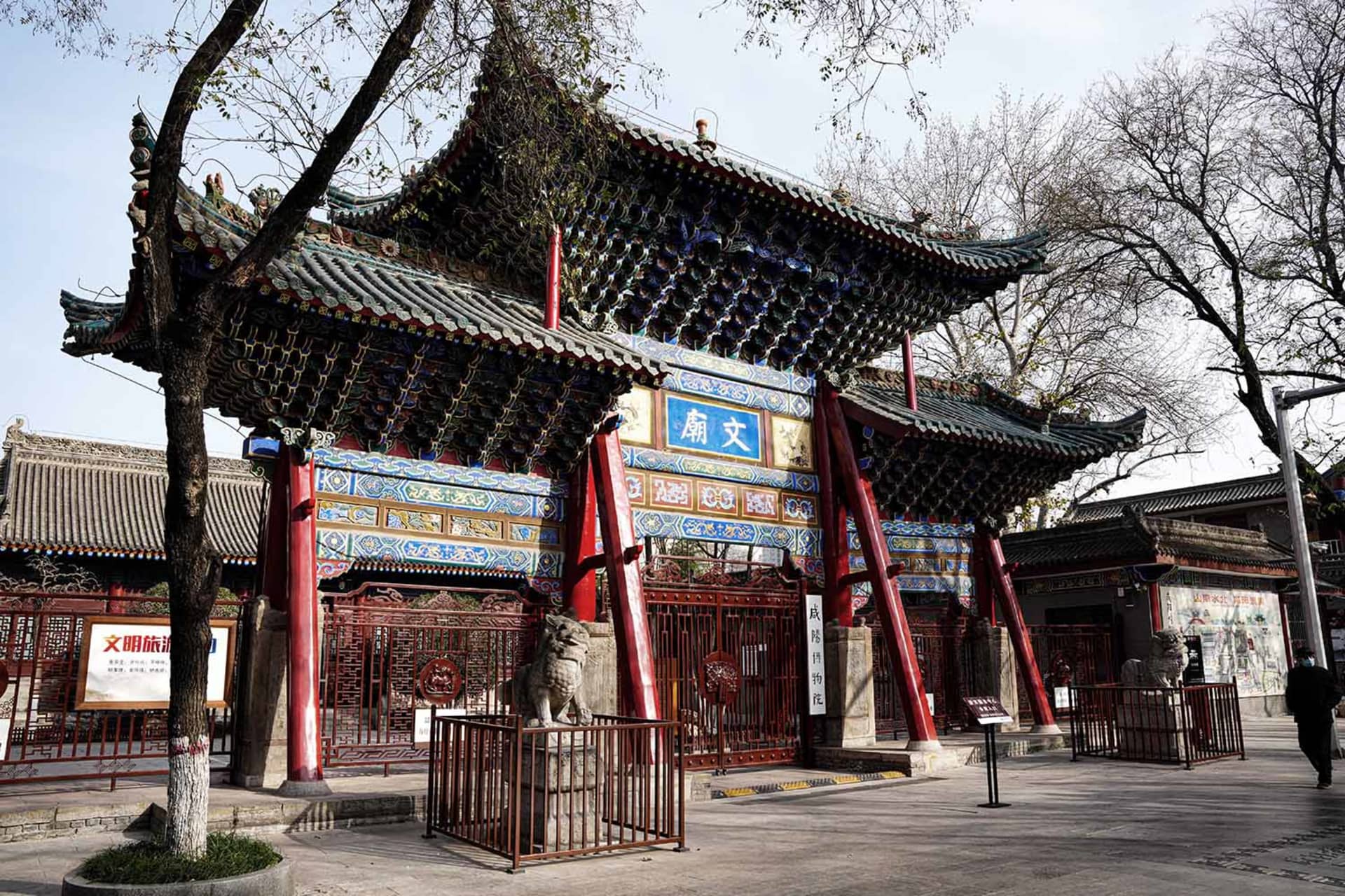 紅牆亞洲風建築，大型門廊入口，以及數尊雕像包括獅子，襯托於文化藝術背景