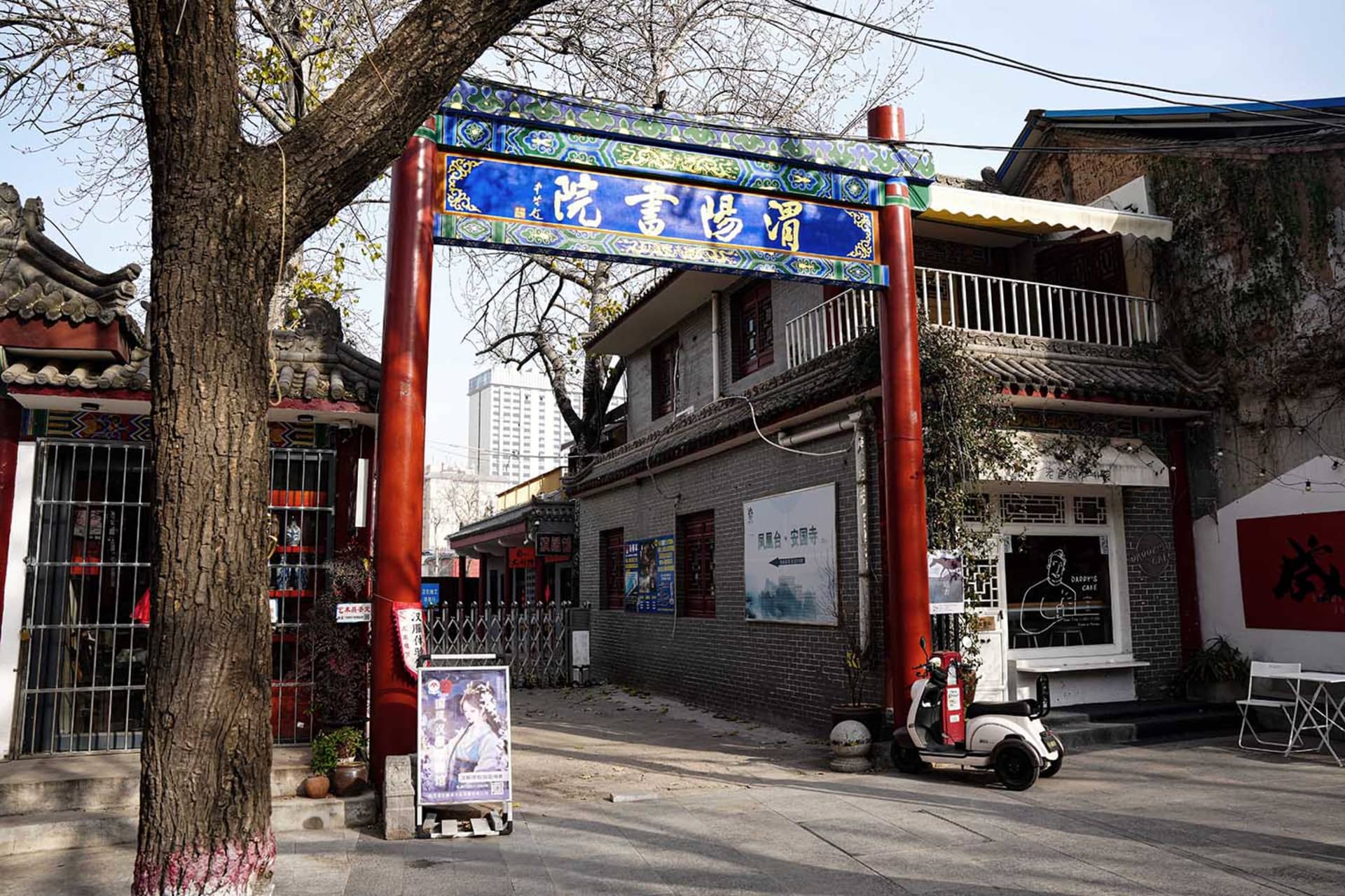 A bustling Asian city street corner with a red building featuring a large archway entrance and signs, surrounded by people and vehicles