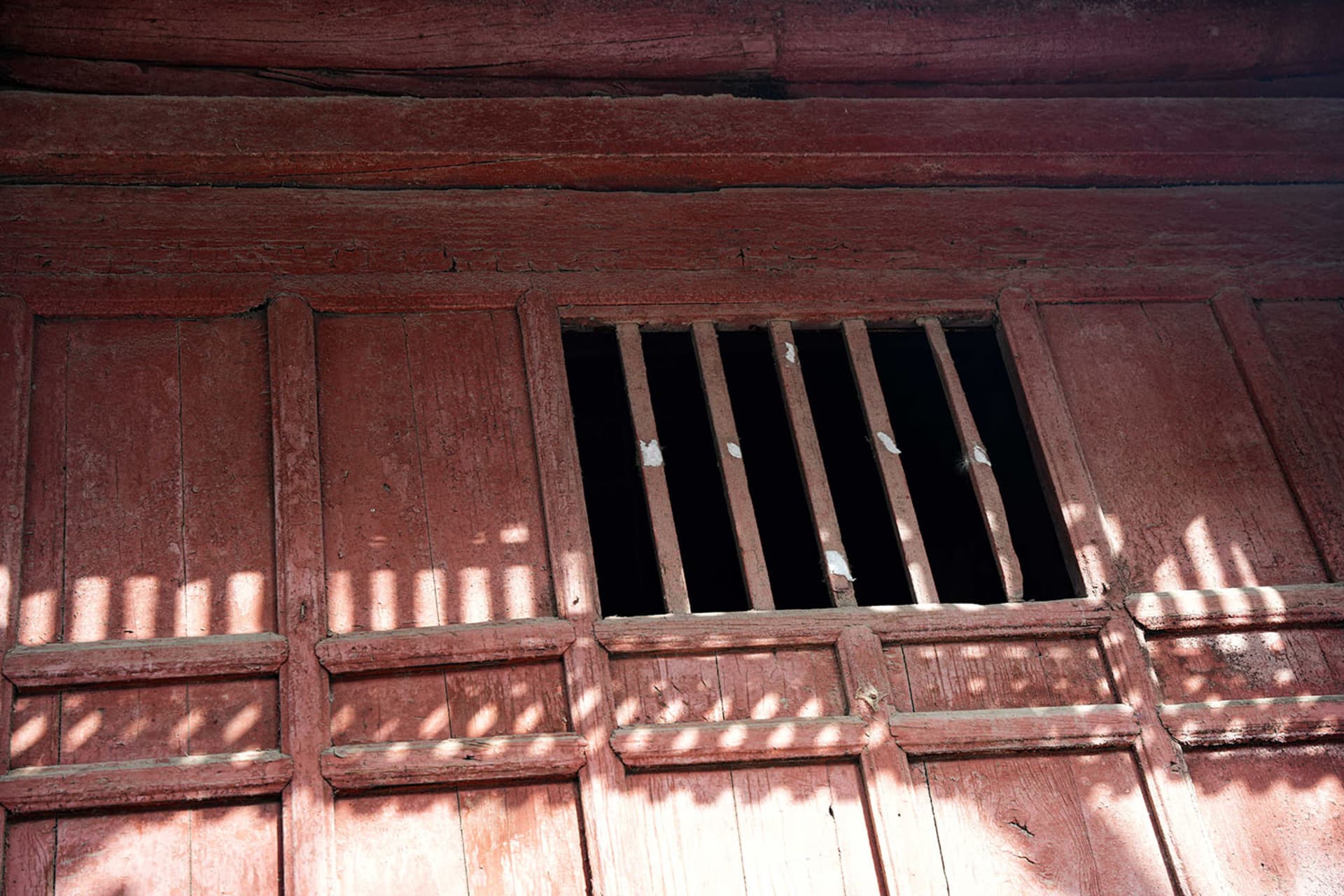 Old red building with a window featuring bars, set against a warm and inviting background