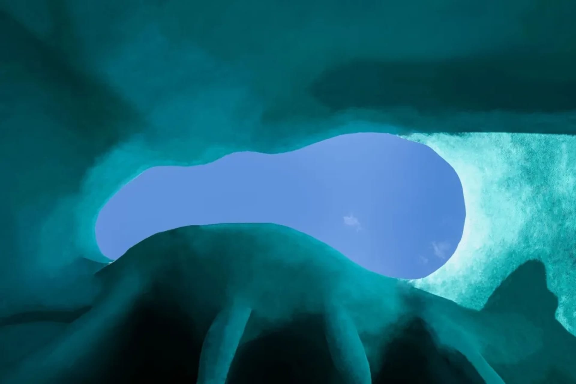 An underwater cave with a large opening leading to a vast underground chamber, surrounded by clear blue water and rugged stone walls