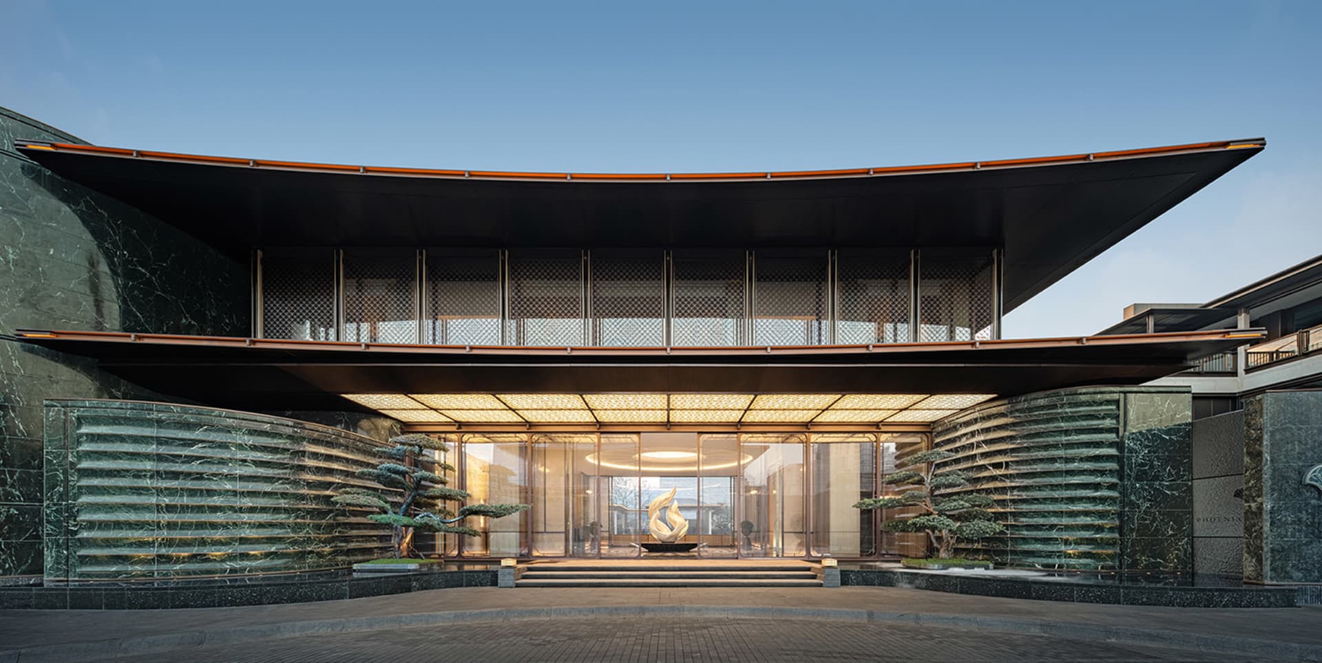 A modern building with a circular shape and a large glass wall featuring a fireplace, surrounded by natural light and a bright atmosphere