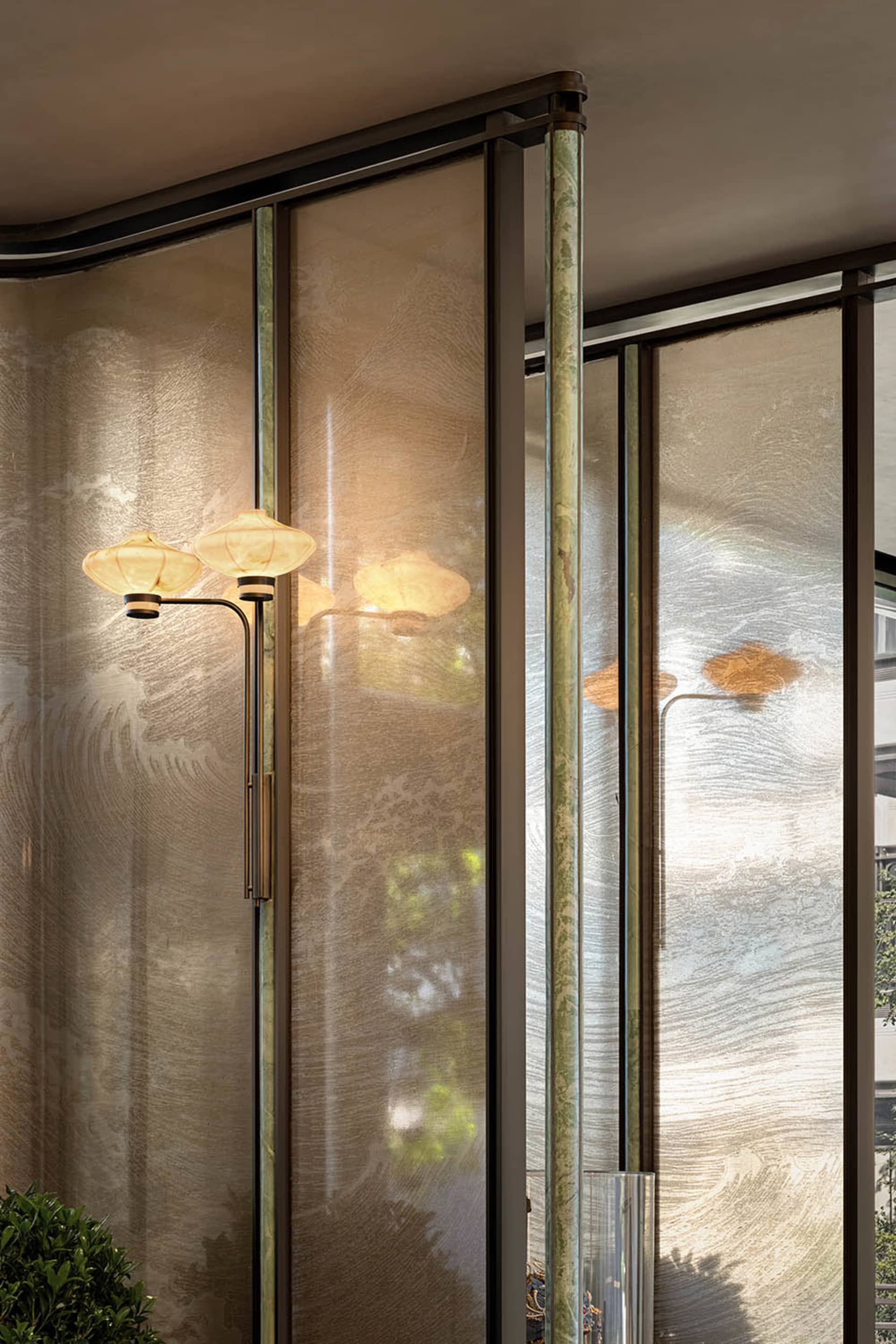 Dimly lit interior space with gold-accented glass doors, frosted glass panels, and a potted plant, featuring three table lamps and a cozy atmosphere