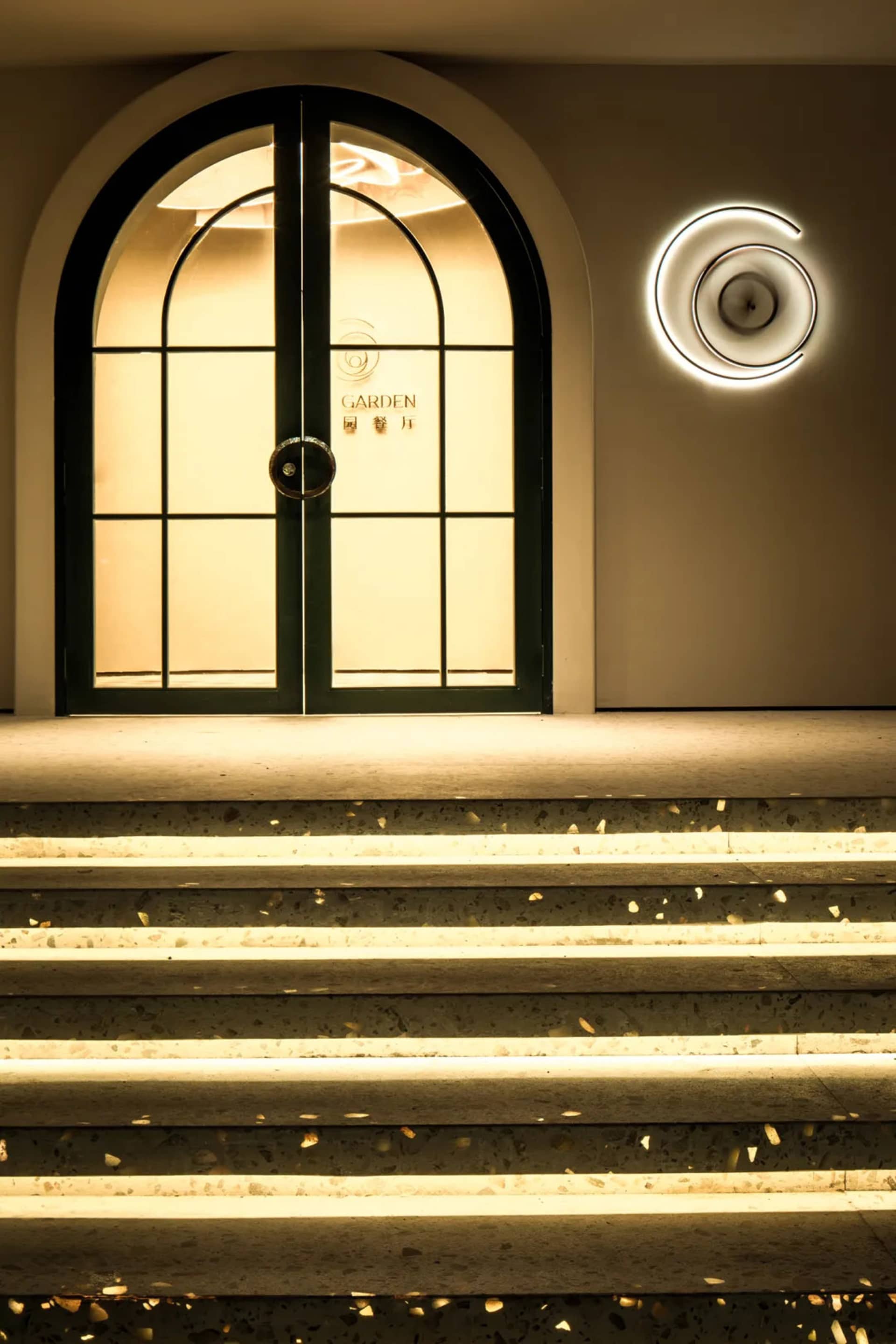 A bright and welcoming entrance with a green door and white wall, illuminated by two circular lights