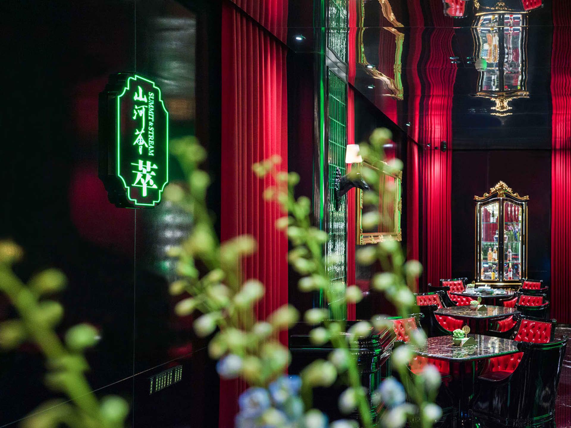Warm and inviting Asian restaurant interior with red walls, green neon lights, chairs, tables, and a bar area with a countertop and decorative items