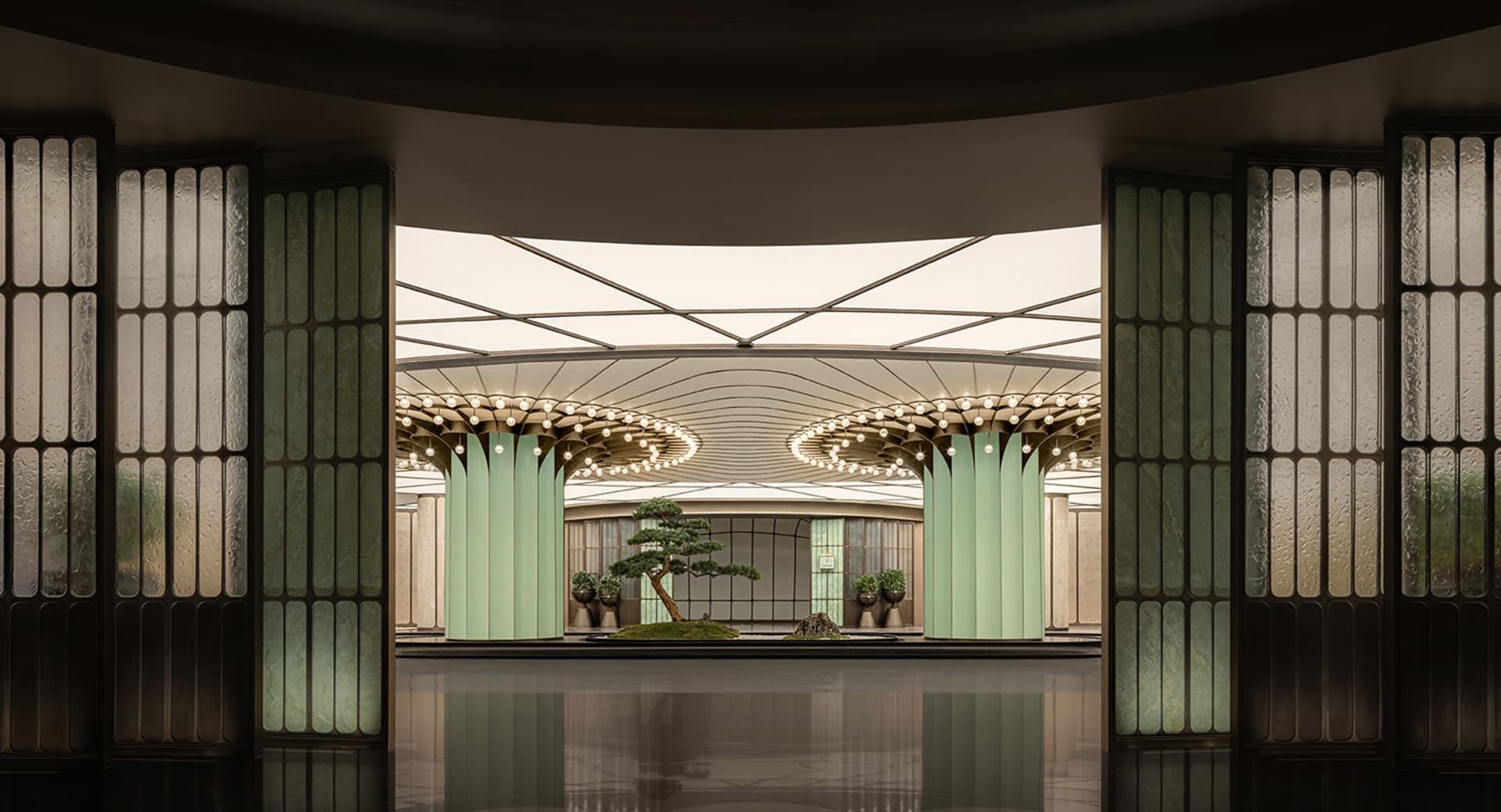 A large building with a green roof and central atrium, surrounded by columns and potted plants, with natural light illuminating the area
