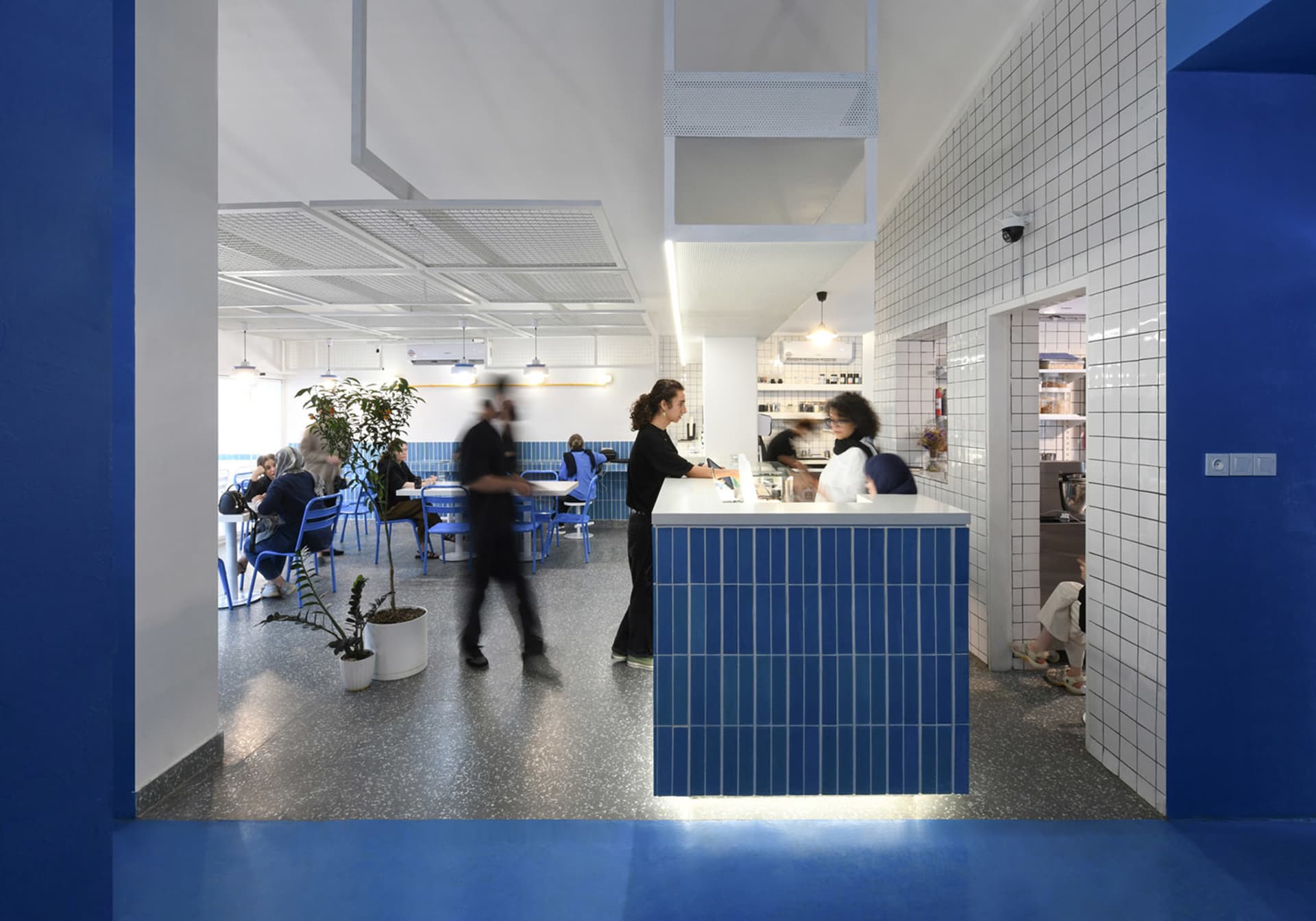 Casual restaurant interior with a blue countertop, blue walls, and modern blue tiles, featuring a bustling atmosphere with people ordering food