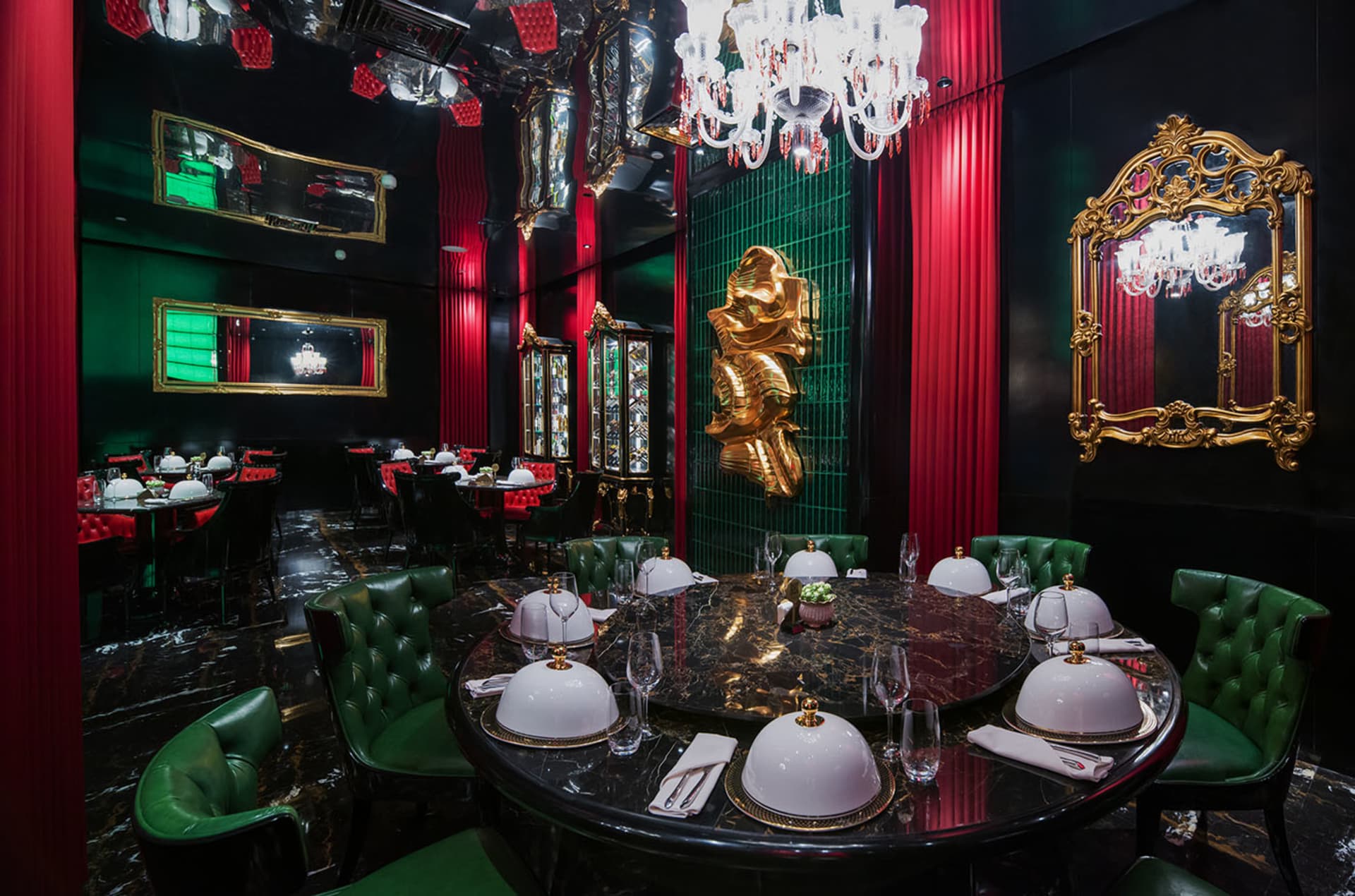 Elegant dining area with a table set for a meal, surrounded by chairs, in a room with red walls and a chandelier