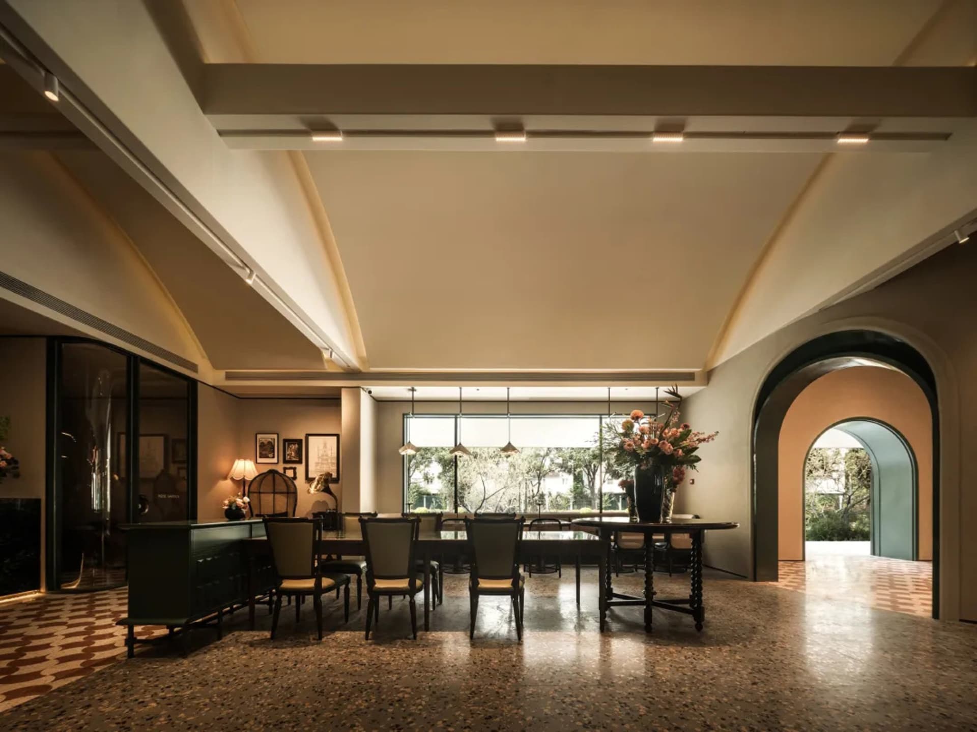 Spacious dining room with a large table, high ceilings, and well-lit atmosphere, featuring a vase of flowers on the table