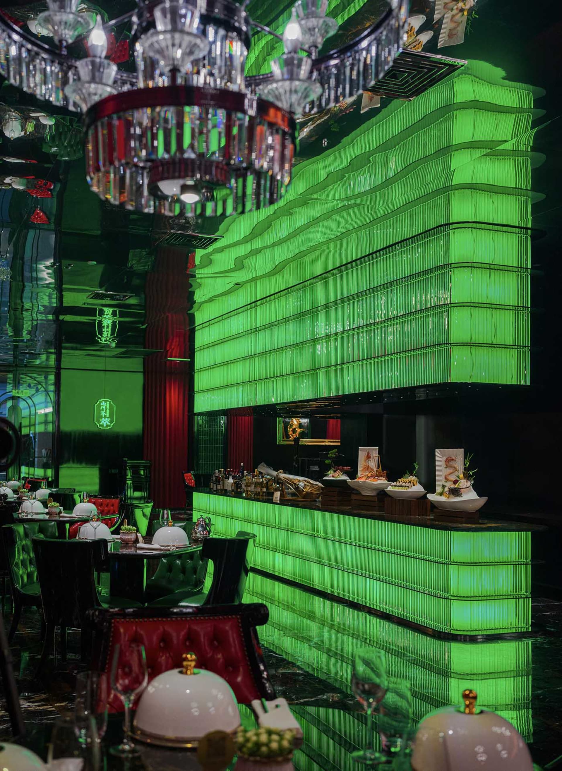 現代餐廳內部，綠色牆面、吧台區，以及鋪白桌布的餐桌與各式碗盤，背景為廚房