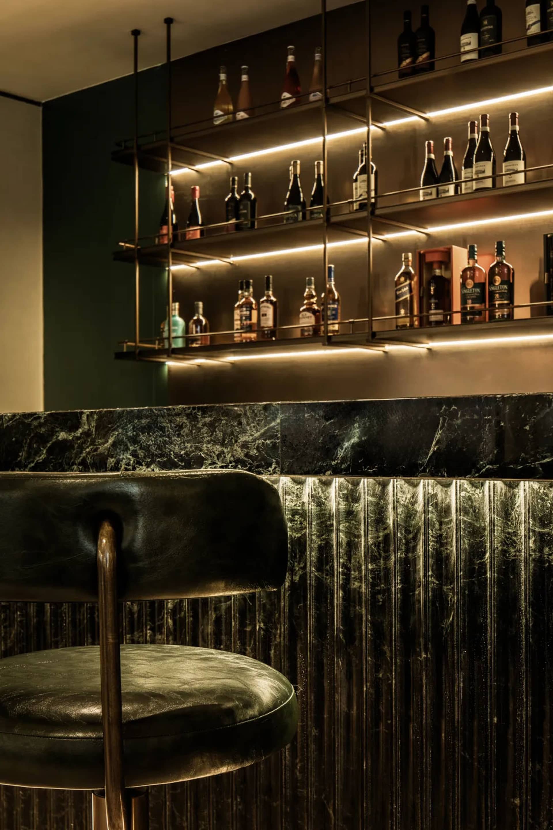 A sophisticated bar area with a black leather chair, marble countertop, and a selection of bottles on display