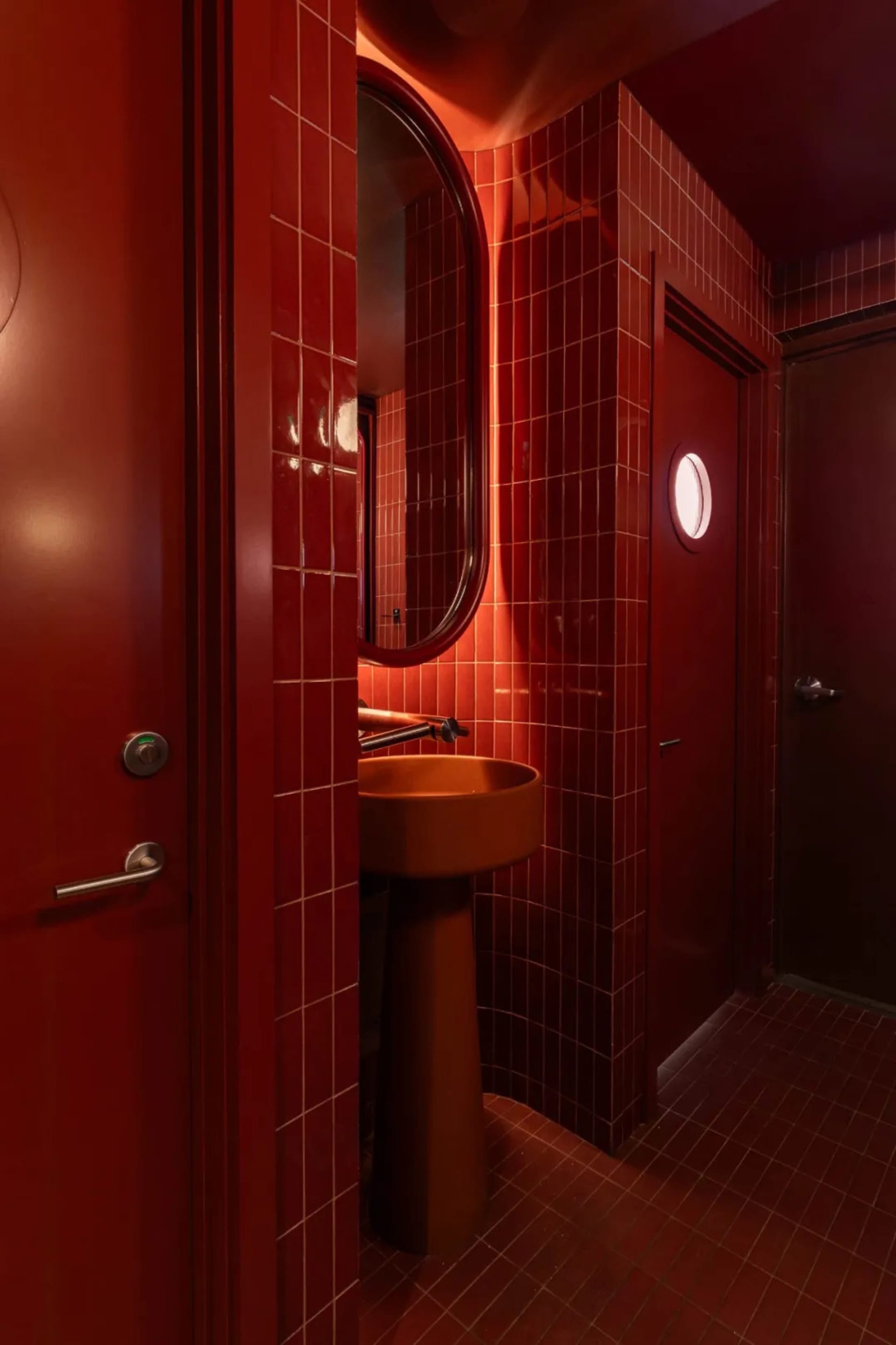 Bathroom with two sinks, one with a mirror, and red walls, set in a well-lit space with natural light