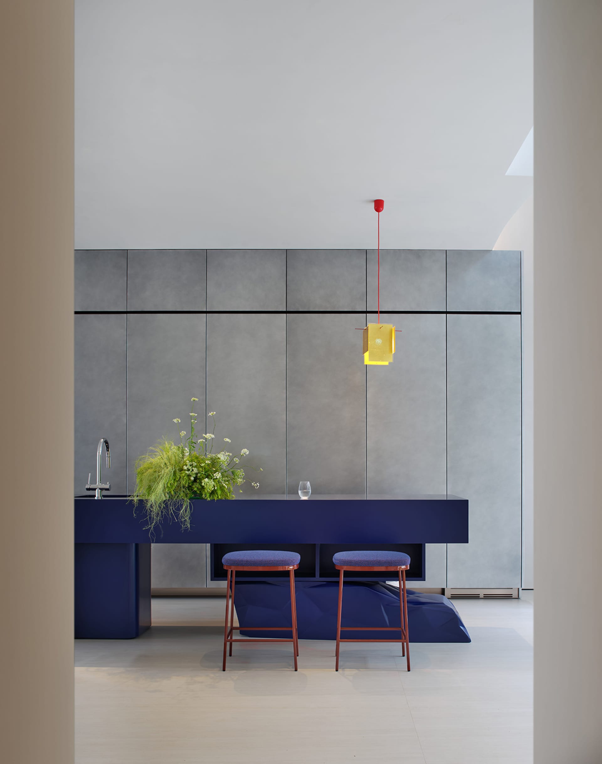 Modern kitchen with a blue countertop, grey walls, a sink, stools, and a potted plant