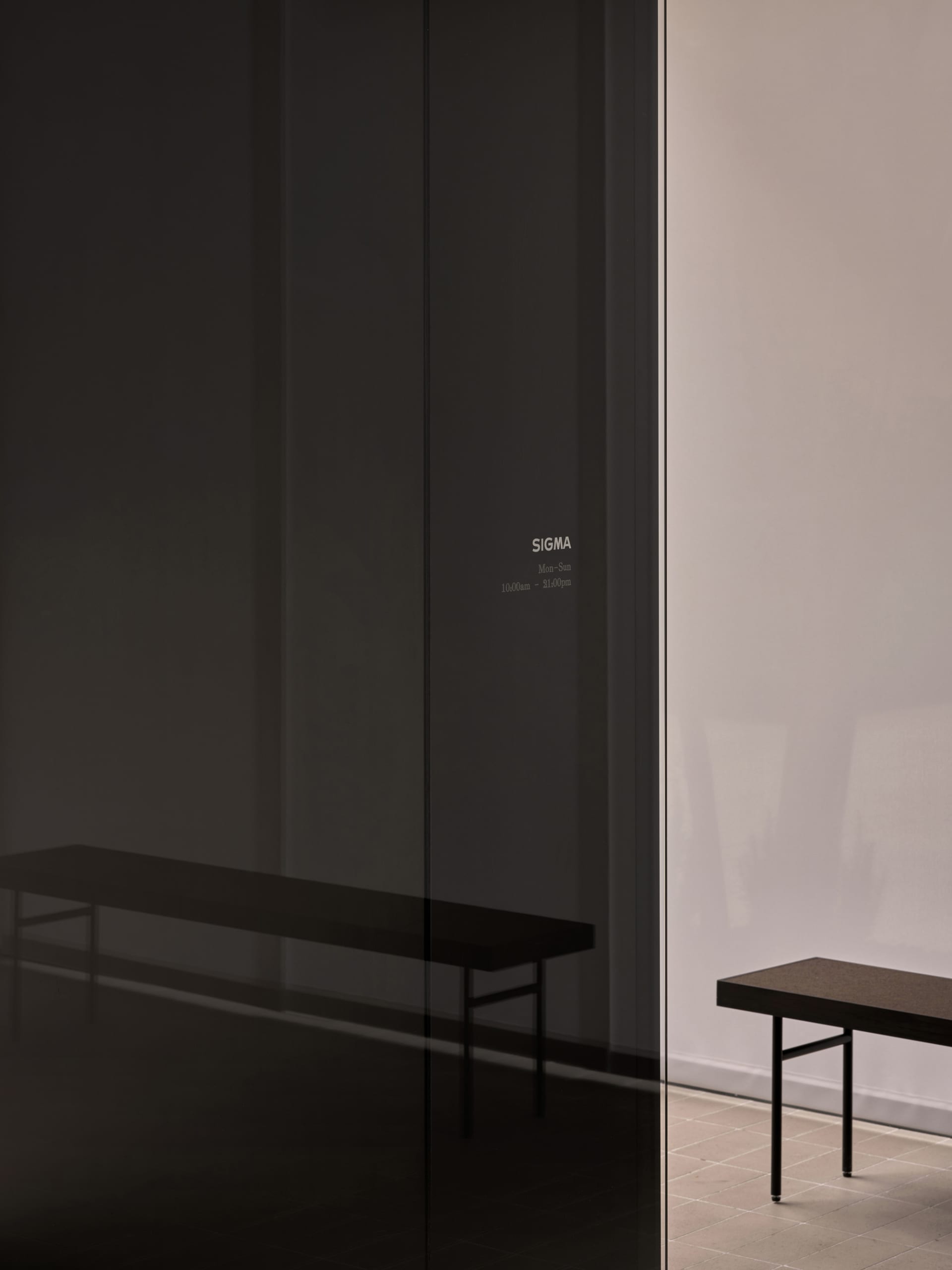 Modern interior space with two tables and a bench in front of a glass wall, featuring clean lines and a minimalist design