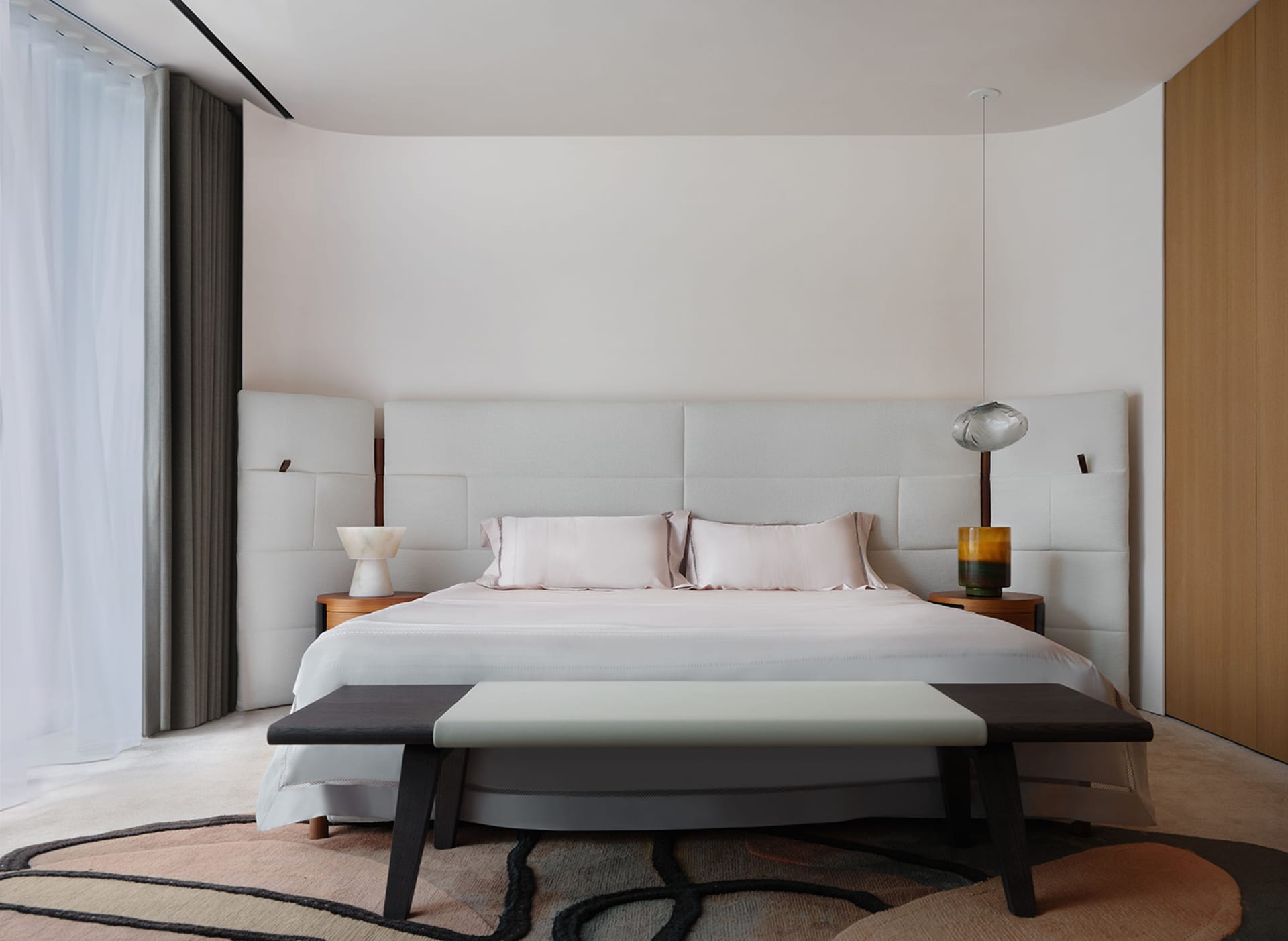 Cozy bedroom with a large white bed, wooden headboard and footboard, and a chair on a hardwood floor