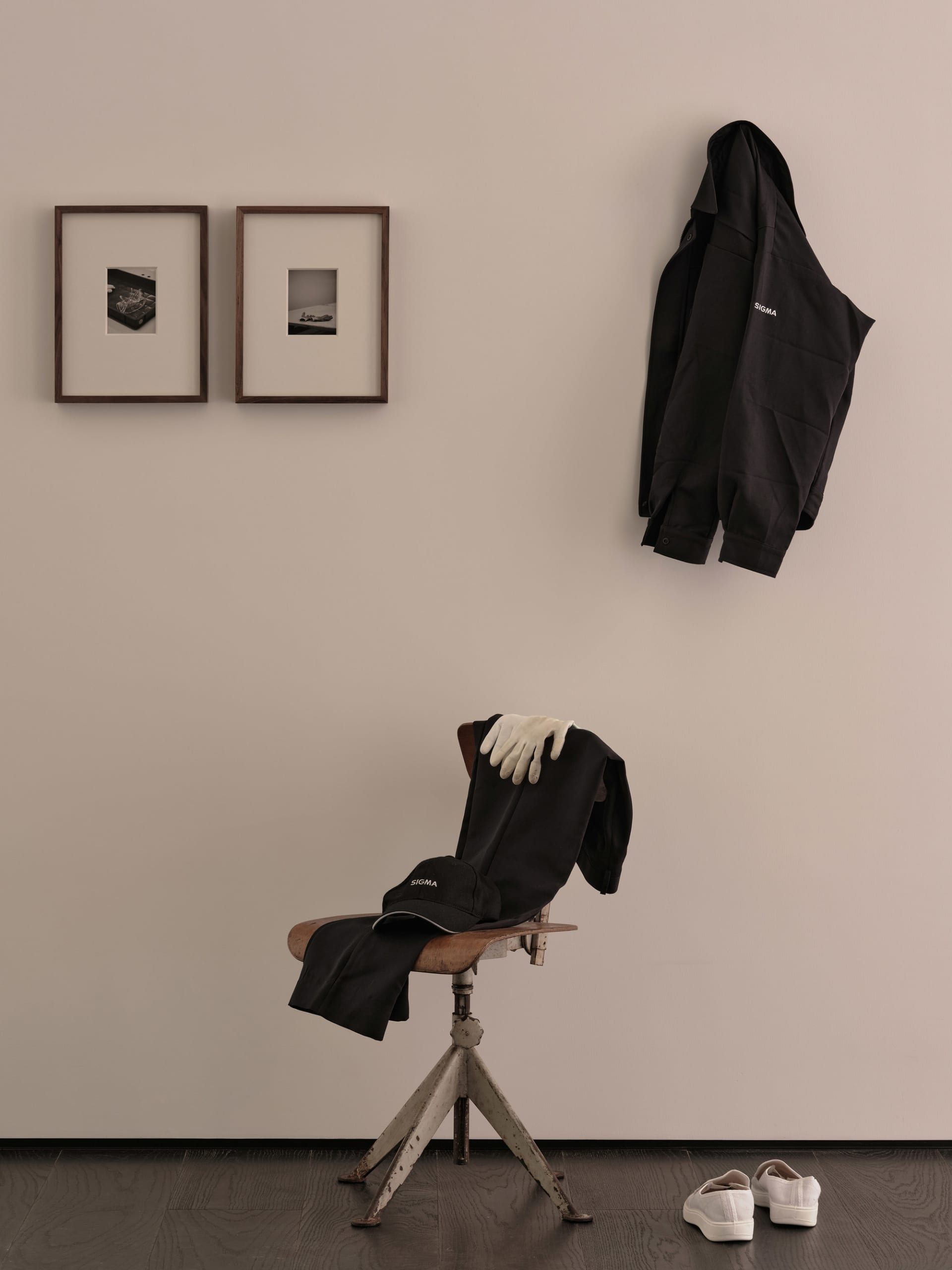 A home office with a white wall featuring two framed pictures and a chair with two black jackets and a handbag