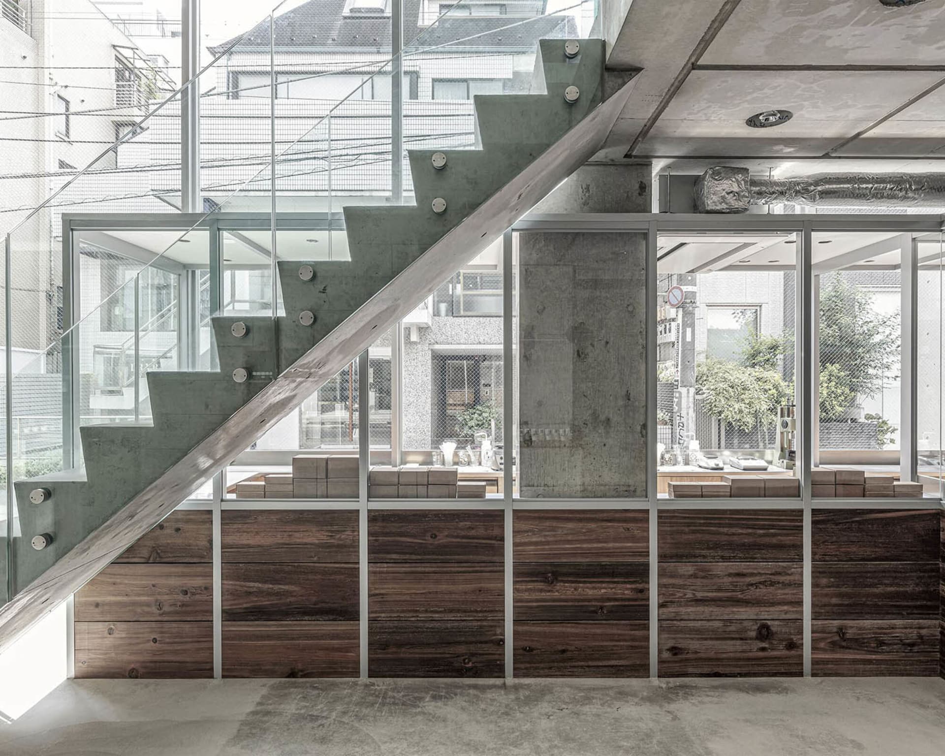 A modern building with a wooden staircase, large windows, potted plants, and decorative vases, set against a bright and airy background