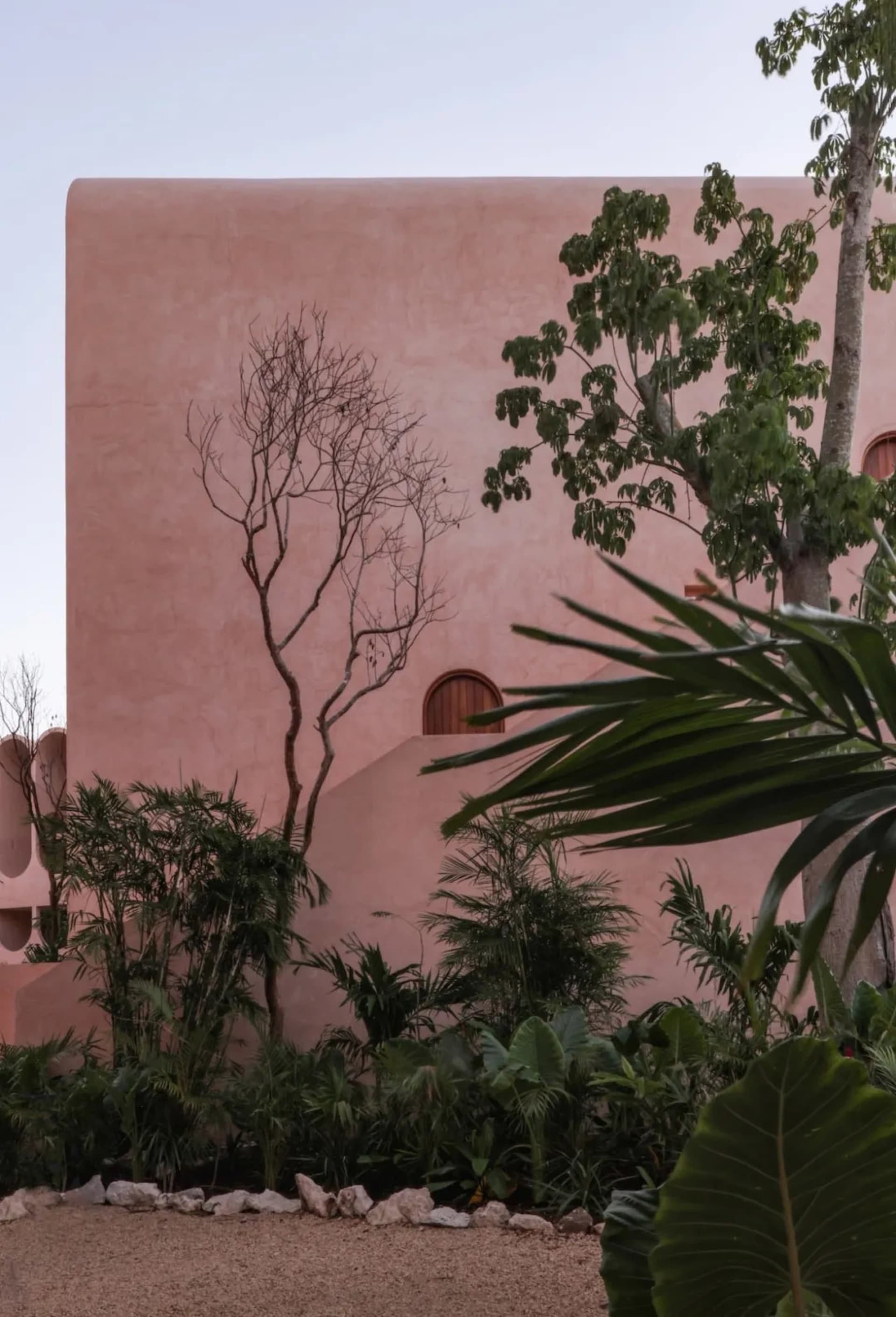 A stone building with a pink facade, surrounded by two trees, in a calm and serene environment