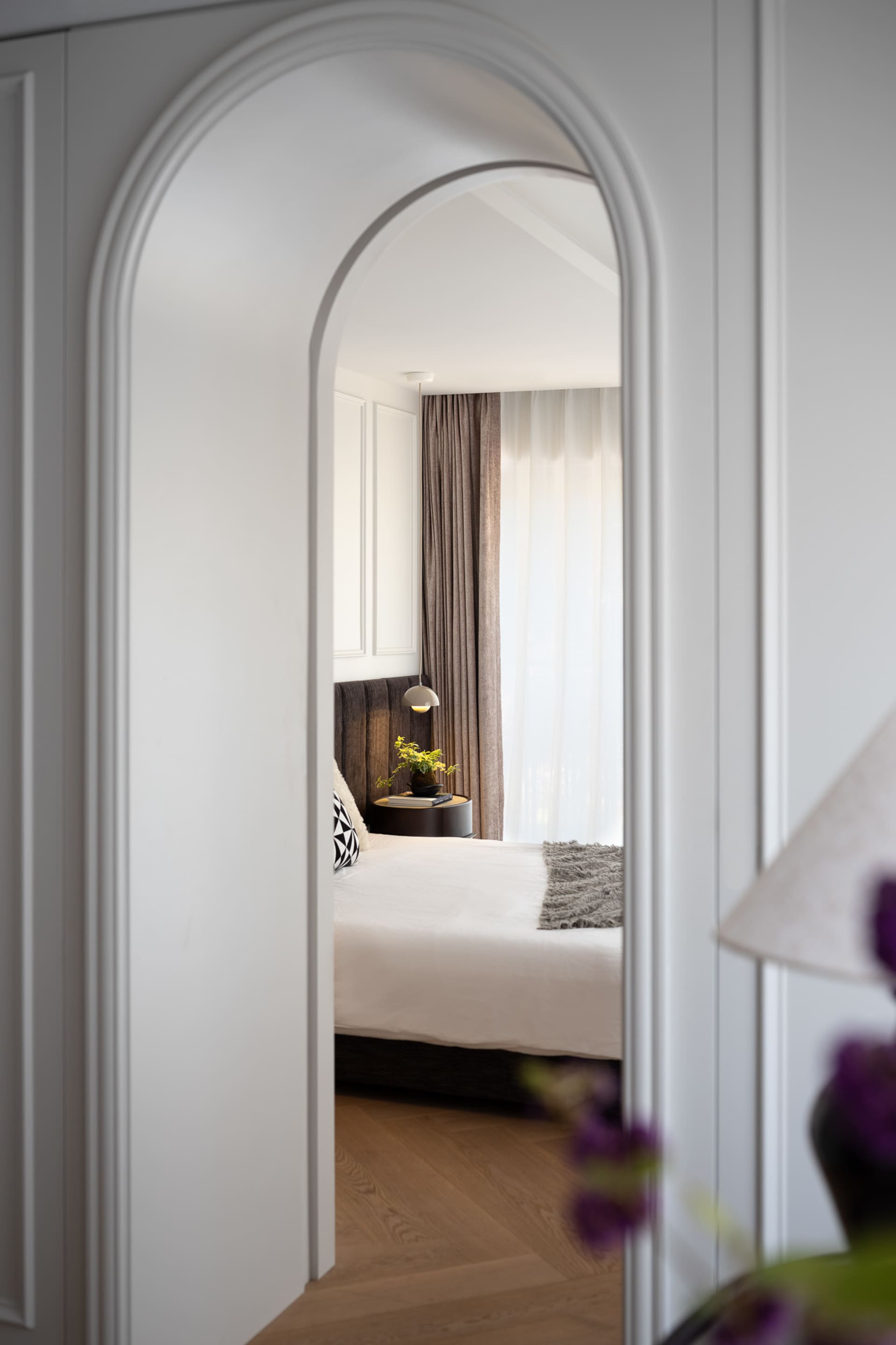 Cozy bedroom with a white bed, black pillows, and ample lighting from two lamps and large windows
