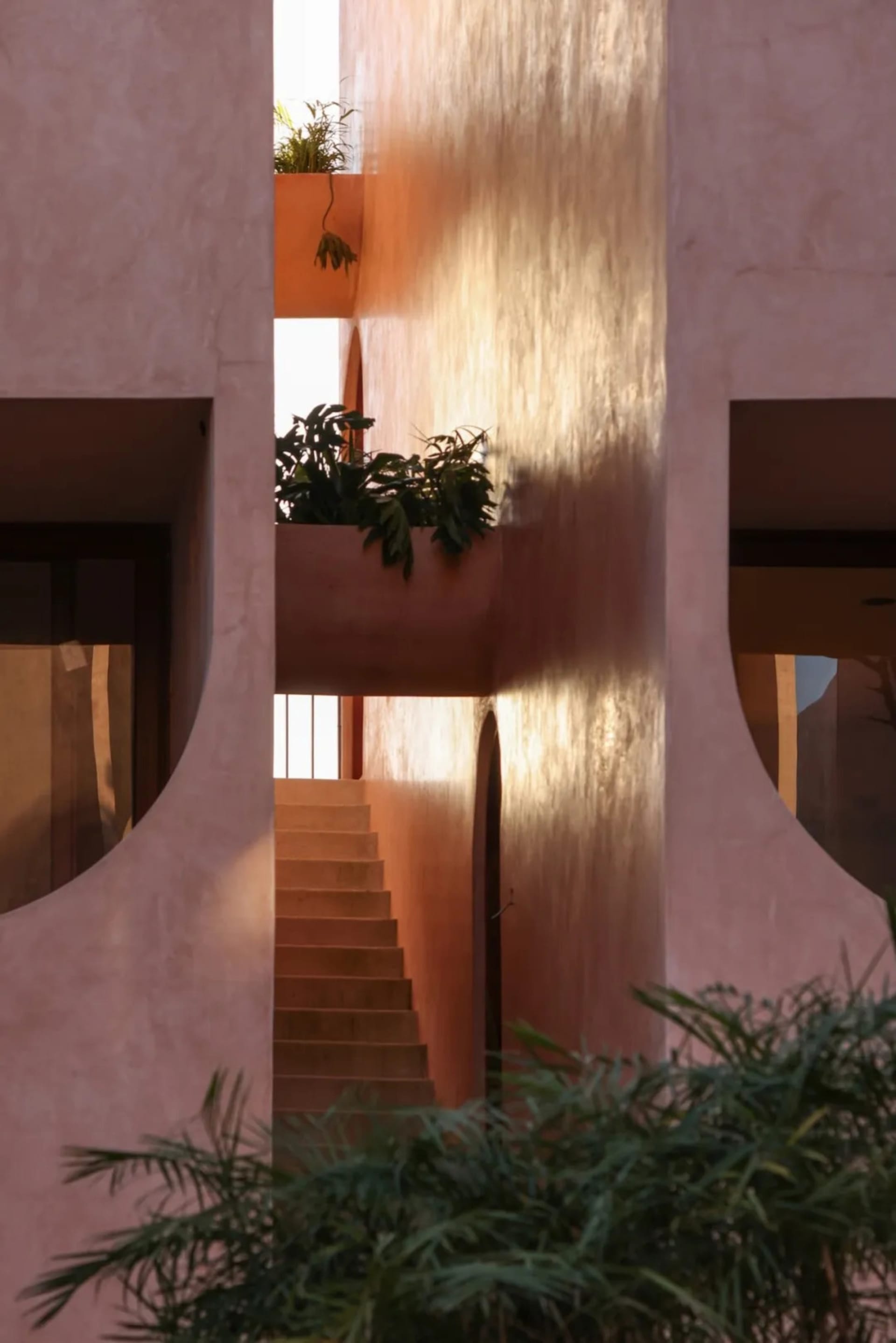 A warm and inviting building with a pink exterior, featuring a staircase leading to a balcony with a plant, and two sets of stairs on either side
