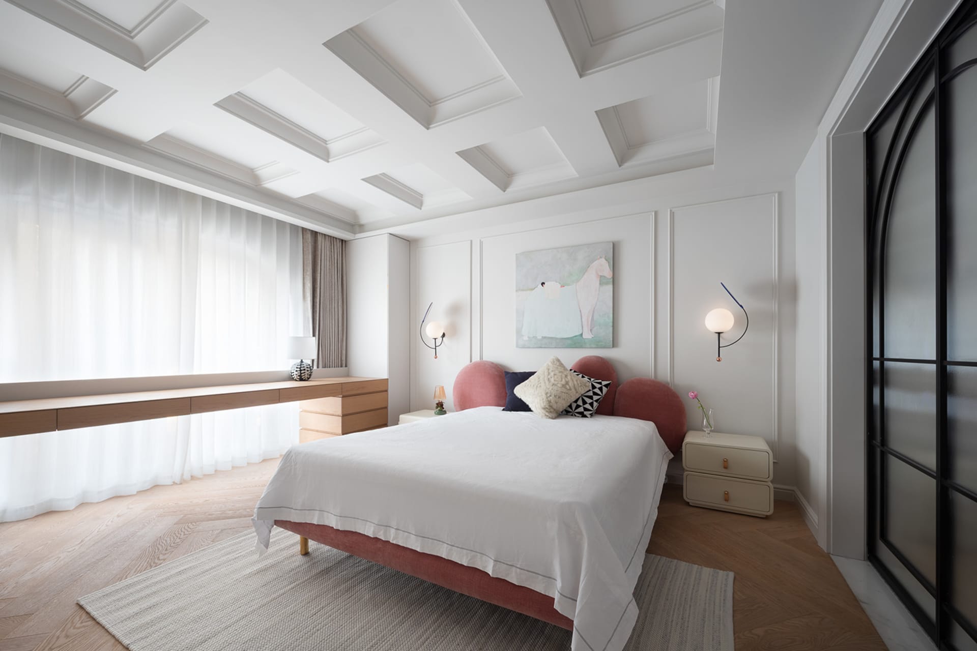 A calm and inviting bedroom with a large white bed, pink headboard and footboard, two nightstands with lamps, a couch, and a chair
