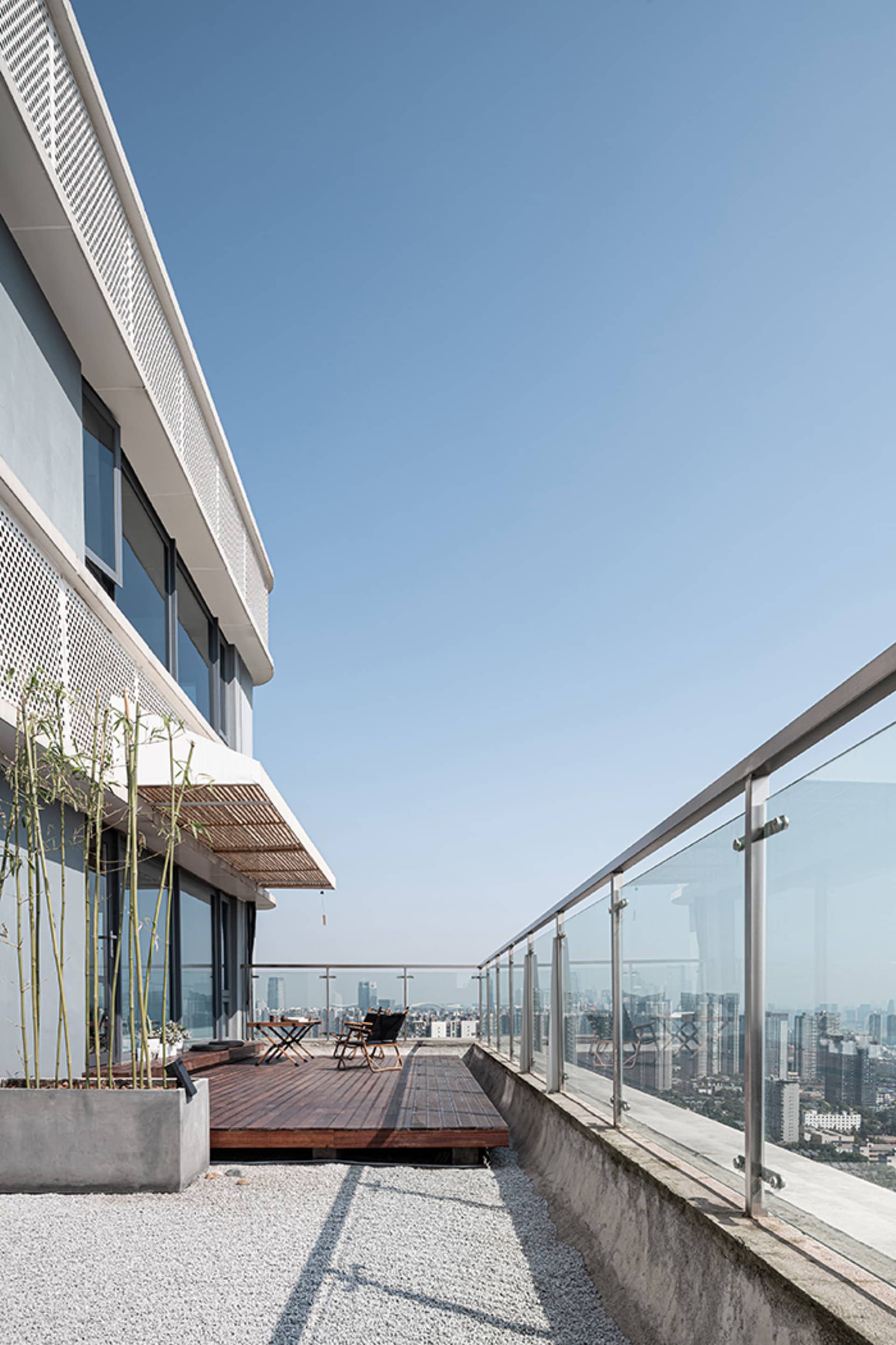 Exterior view of a modern building with a balcony featuring two chairs, a glass railing, and a concrete structure